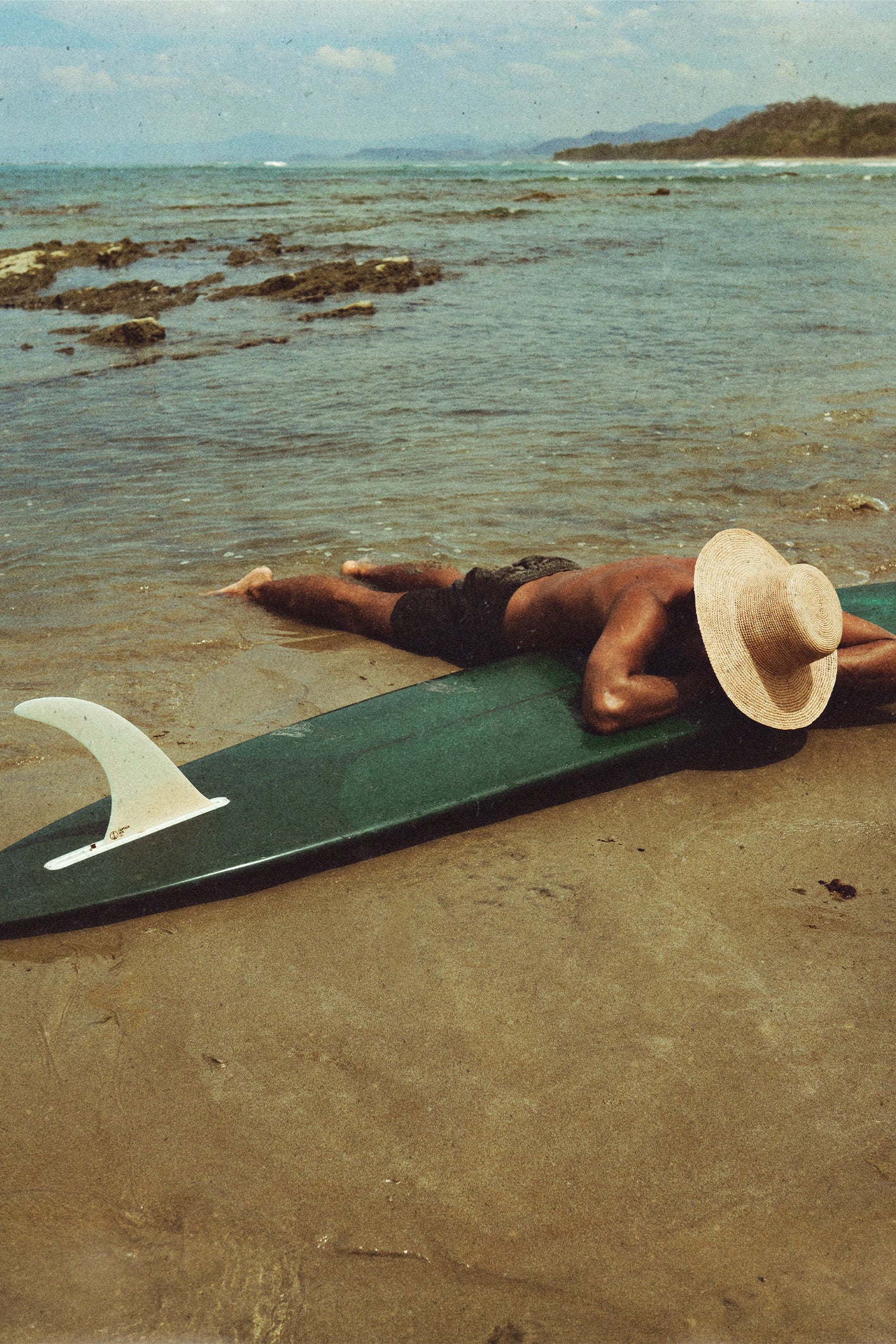 A man lies face-down on the shore on his surfboard in Santa Teresa, Costa Rica, captured in warm, vintage tones by travel photographer Ez Rivero.