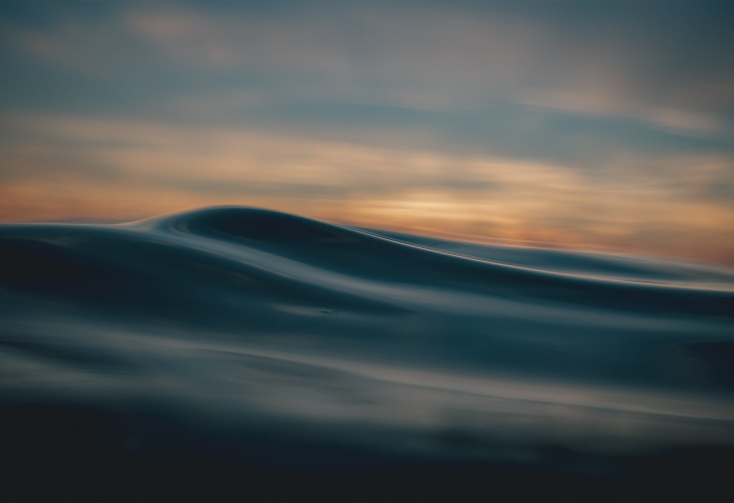 Smooth, abstract ocean wave at sunset under soft golden skies, photographed at Fistral Beach from the sea by Chris Hall.