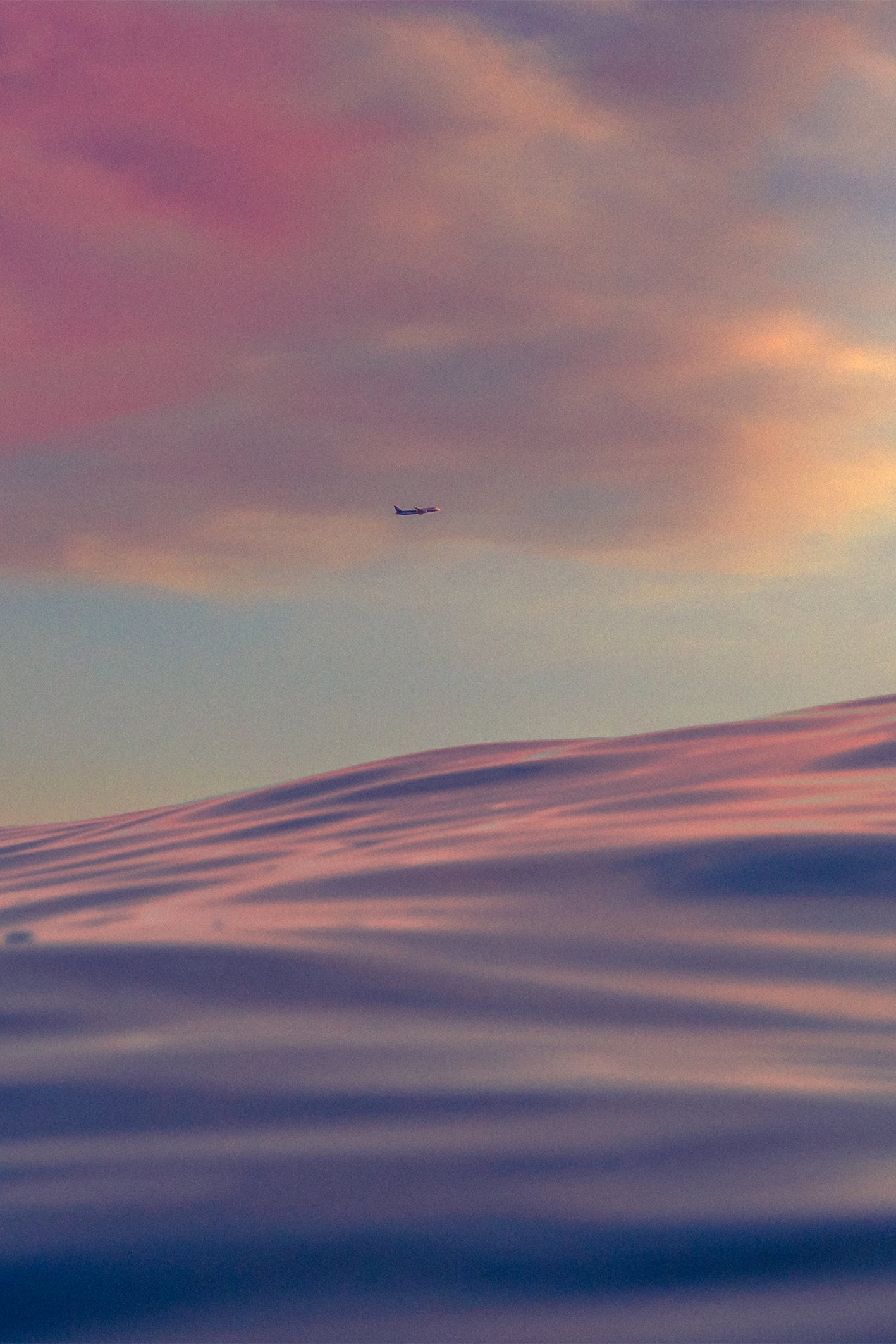 A lone airplane flies across a pastel-hued sunset sky over softly lit sand dunes at Venice Beach, photographed by Craig Hubbard.