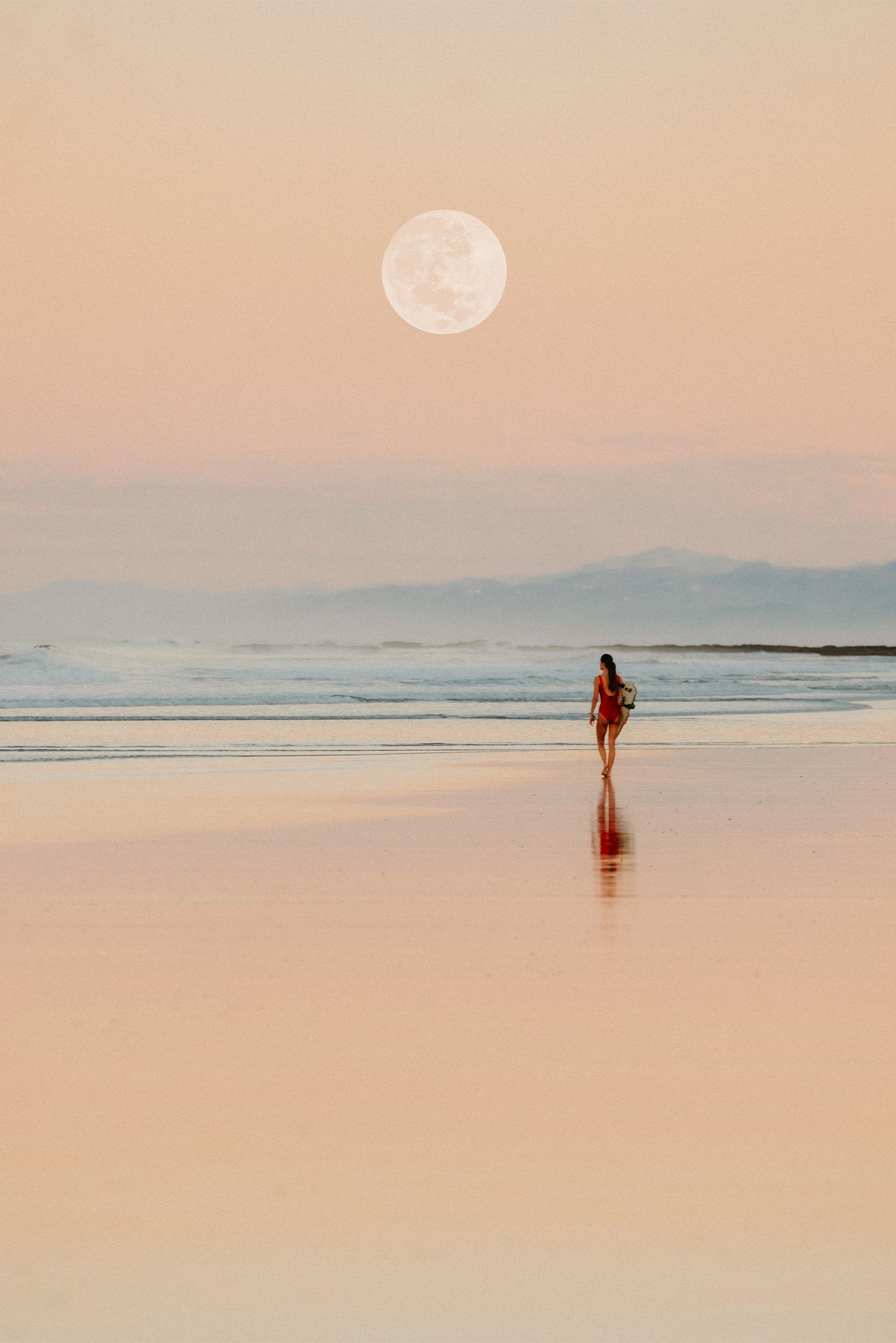 A surfer in a red wetsuit walking towards the surf under the full moon at sunrise - a fine art print by Evie Johnstone from Santa Teresa in Costa Rica.