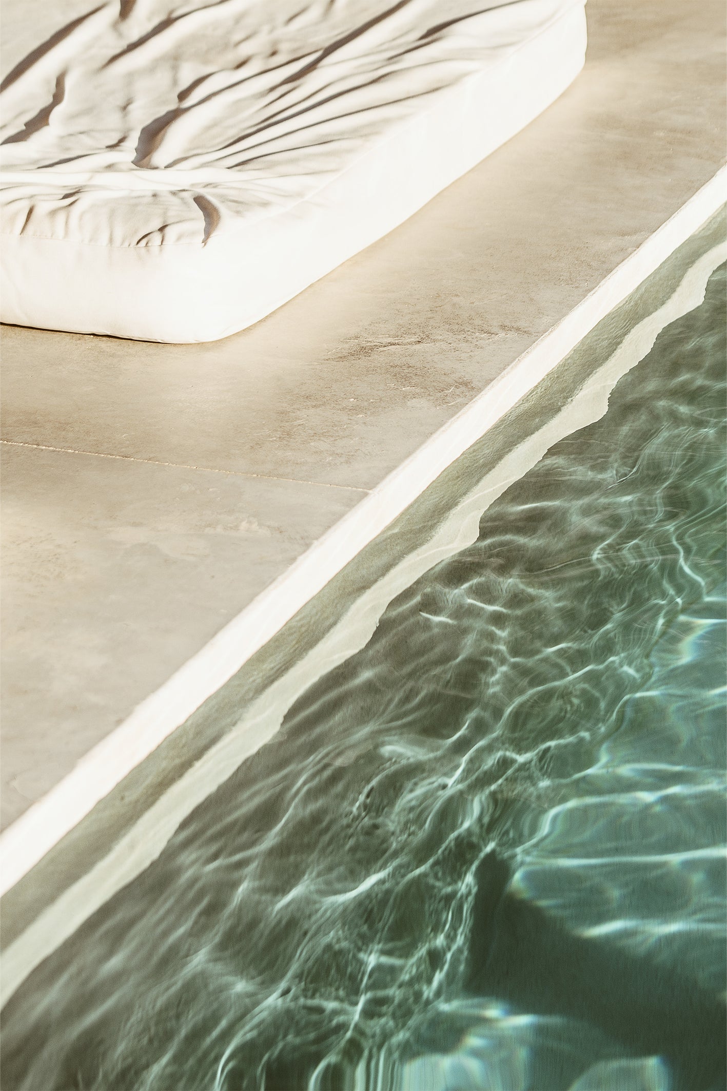 Close-up of a pool edge with stone tiles and turquoise pool water rippling nearby, a calming photography print by Evie Johnstone.