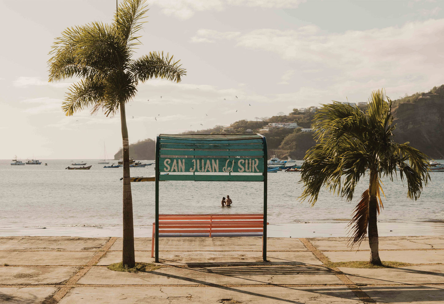 A ready-to-hang fine art photography print by Hannes Kläger, depicting one of the colourful benches that sit beneath swaying palms on the beachfront. Every bench is framed by hand-painted signs that reflect the town’s vibrant spirit.