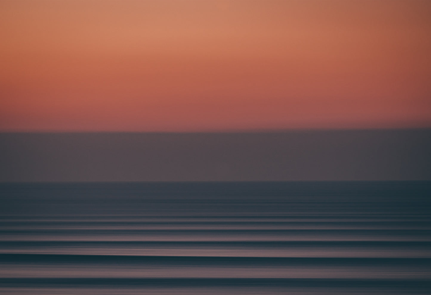 Long-exposure photograph of a moody Atlantic sunset at Fistral Beach, Cornwall, showing abstract horizontal waves beneath a deep red and purple sky.