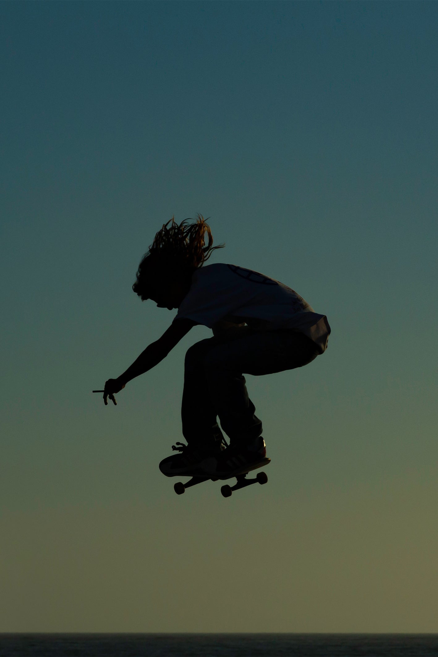 Iconic skateboarding photo of a silhouetted skater with a lit cigarette, catching air at Venice Skatepark - SMOKE by Craig Hubbard, shot at golden hour.