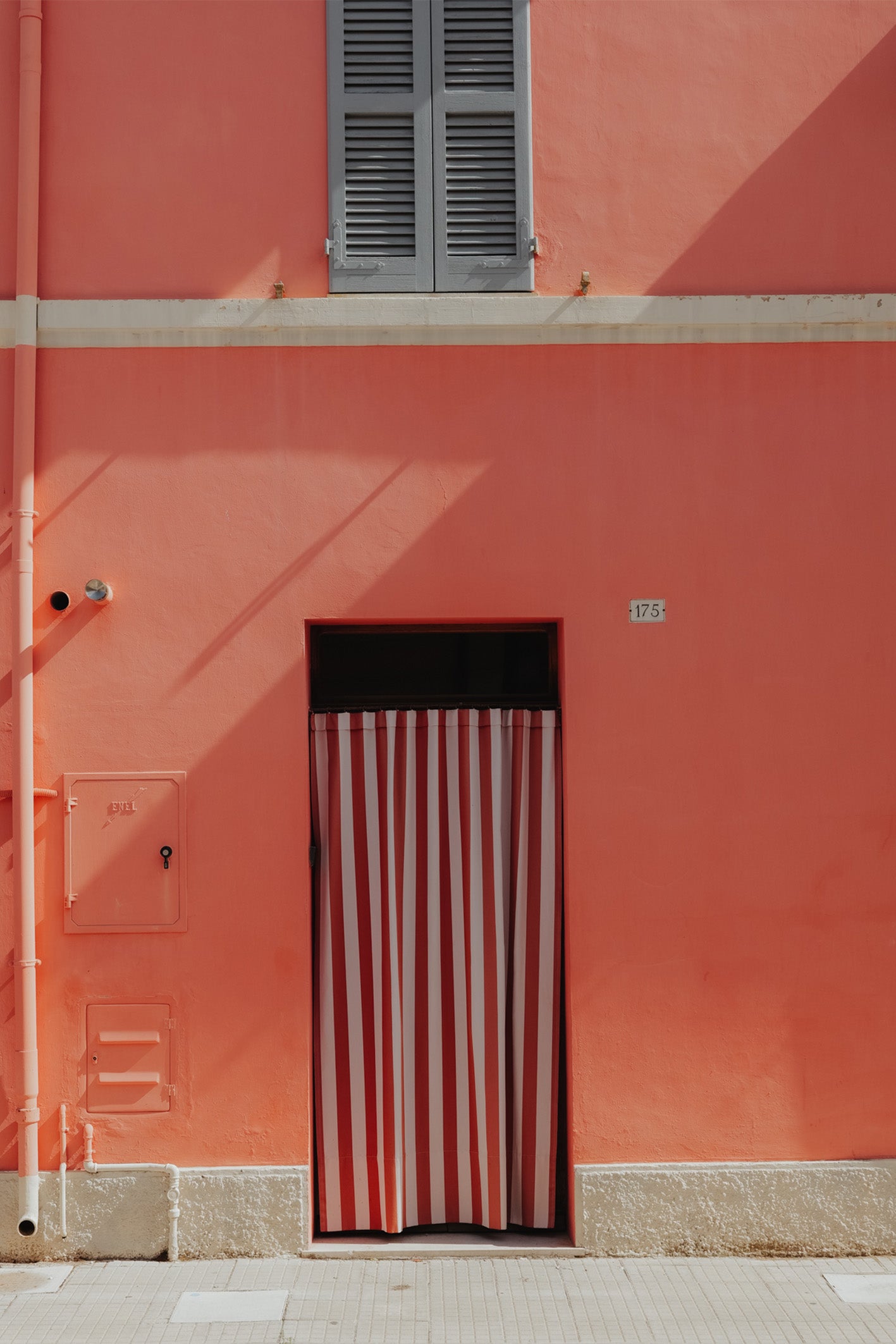 A photograph by Hannes Kläger of a red and white striped curtain on a pink building in the small village of Porto Recanati, Italy. Available to buy as a framed, ready-to-hang fine art print.