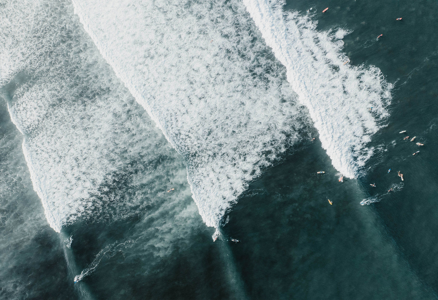 An aerial shot of surfers riding turquoise waves off the coast of Bali, captured in a travel-inspired fine art photograph by Sam Morris.