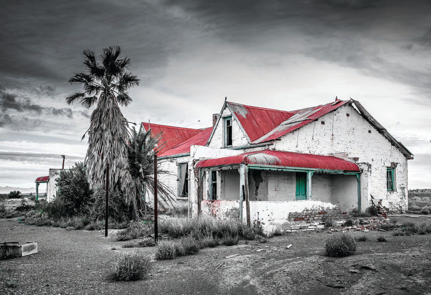 An abandoned farmhouse still stands in the Karoo, with a corrugated red roof and turquoise windows. A striking contrast against the rugged landscape. A fine art photography print by Charles Johnstone, available framed and ready-to-hang on The Lost Works.