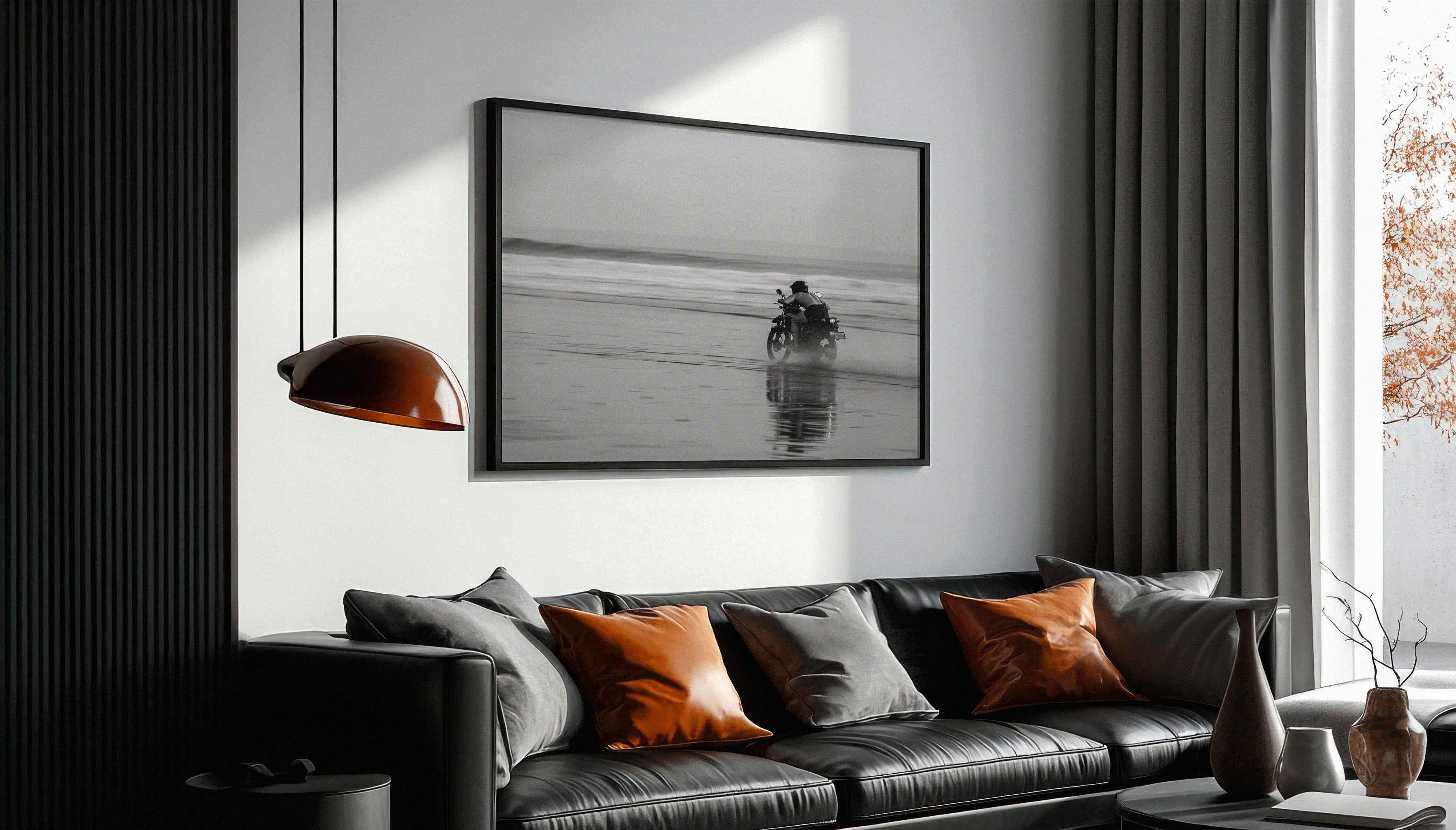 Sam Morris' fine art black & white photography print depicting a motorbike rider kicking up sand on a beach at dusk in Bali, with blurred waves in the background., shown in a black frame above a black sofa.