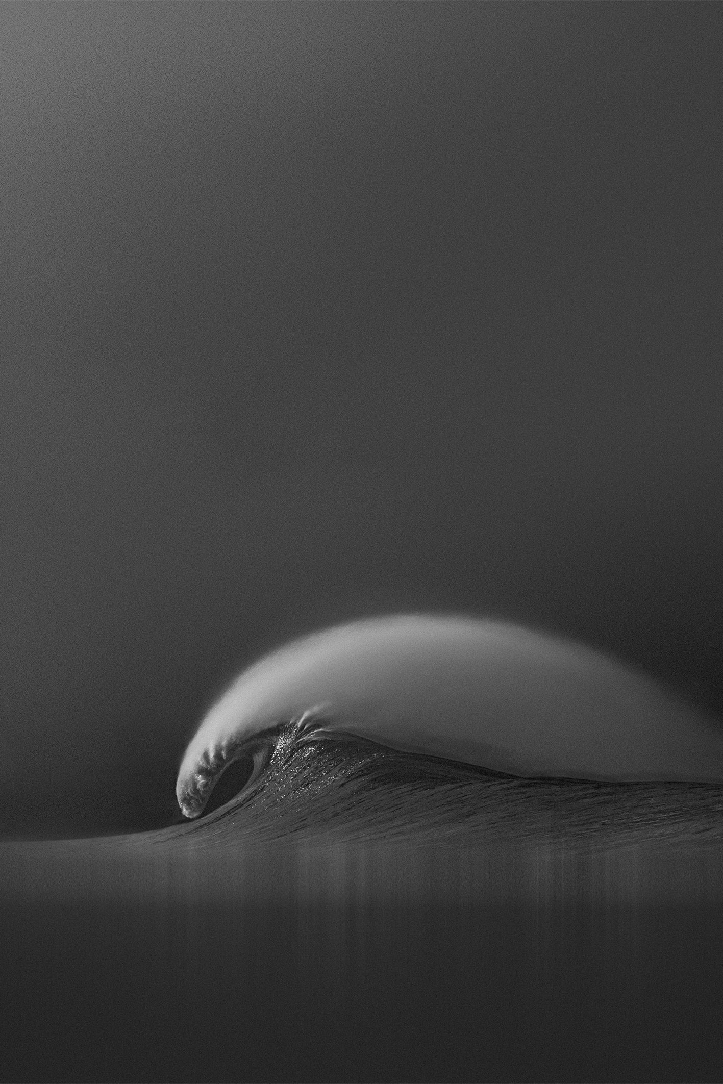 A black and white photograph by Craig Hubbard capturing a perfectly arched ocean wave at Manhattan Beach, with soft textures and moody atmosphere.