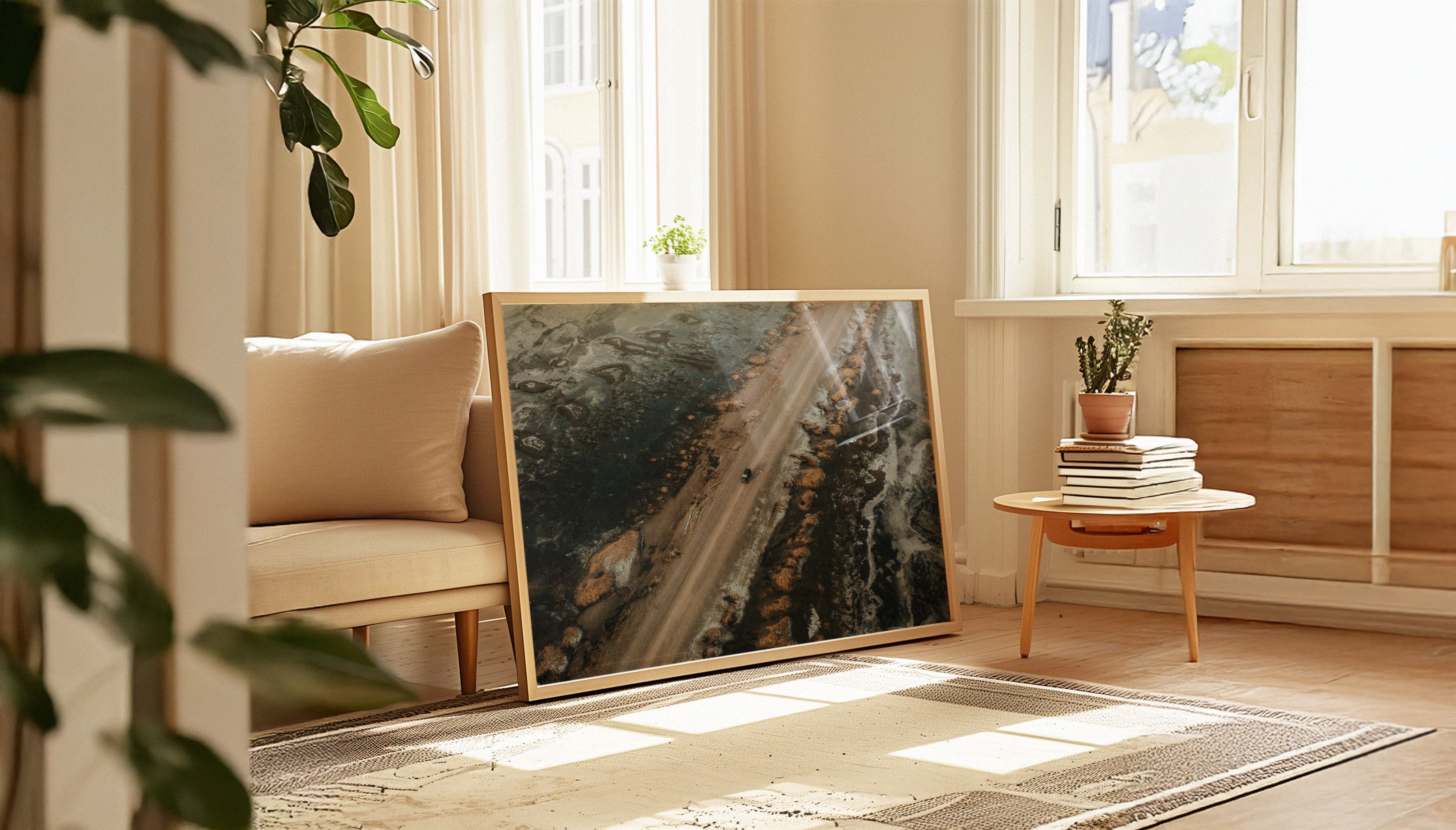 Fine art travel photograph by Sam Morris shown in a large wooden frame, depicting a dusty road in Iceland flanked by golden rocks with patches of snow, surrounded by deep blue water reflecting sky and ice.