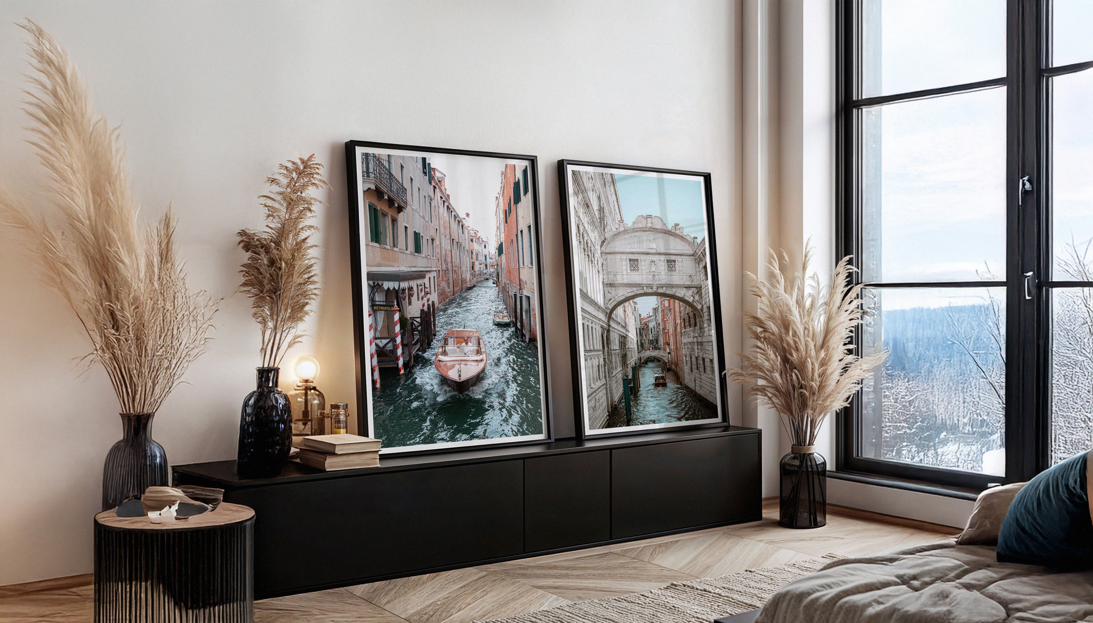A pair of black frames in a Scandi-style living room, showing two of Charles Johnstone's pastel coloured fine art prints 'Cruising in Venice' and 'Venice Bridge of Sigh'.