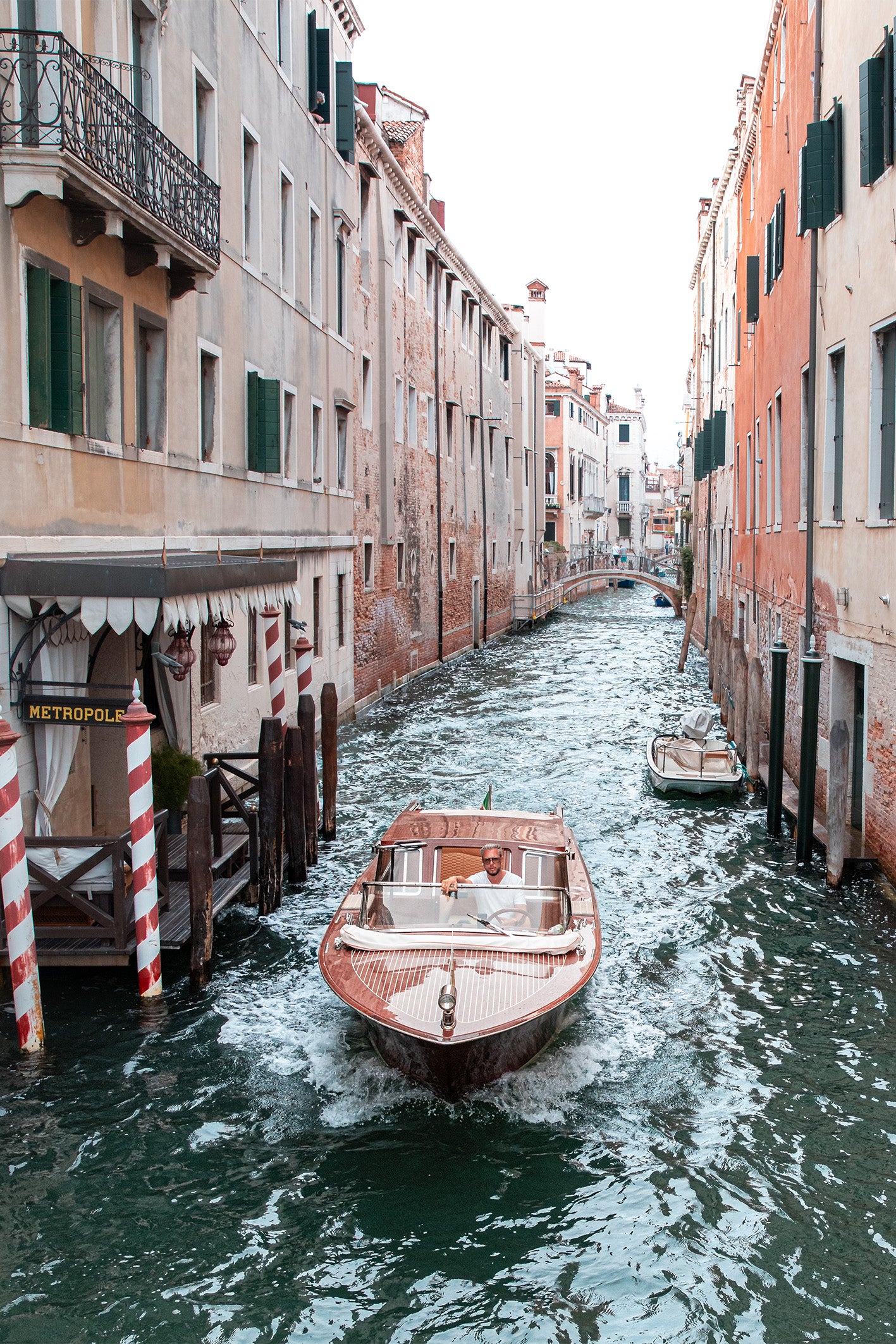 A fine art photography print in pastel colours by Charles Johnstone, depicting a water taxi in Venice being driven by a man who encompasses the laidback Italian vibe.