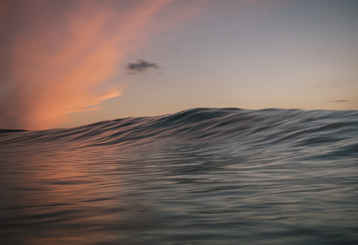 Sunset-lit ocean wave reflecting fiery pink and peach skies off the Cornish coast, photographed by Chris Hall on Fistral Beach, Cornwall.