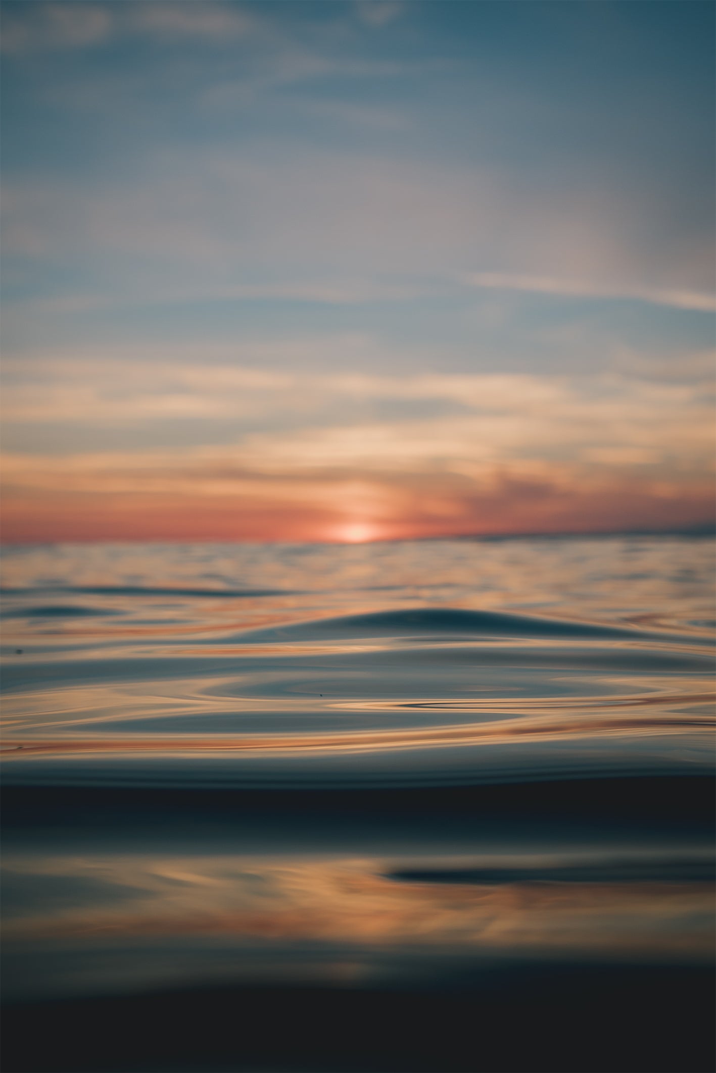 Sunset over a calm ocean with golden light reflecting on smooth water, photographed by Chris Hall in Newquay, Cornwall.