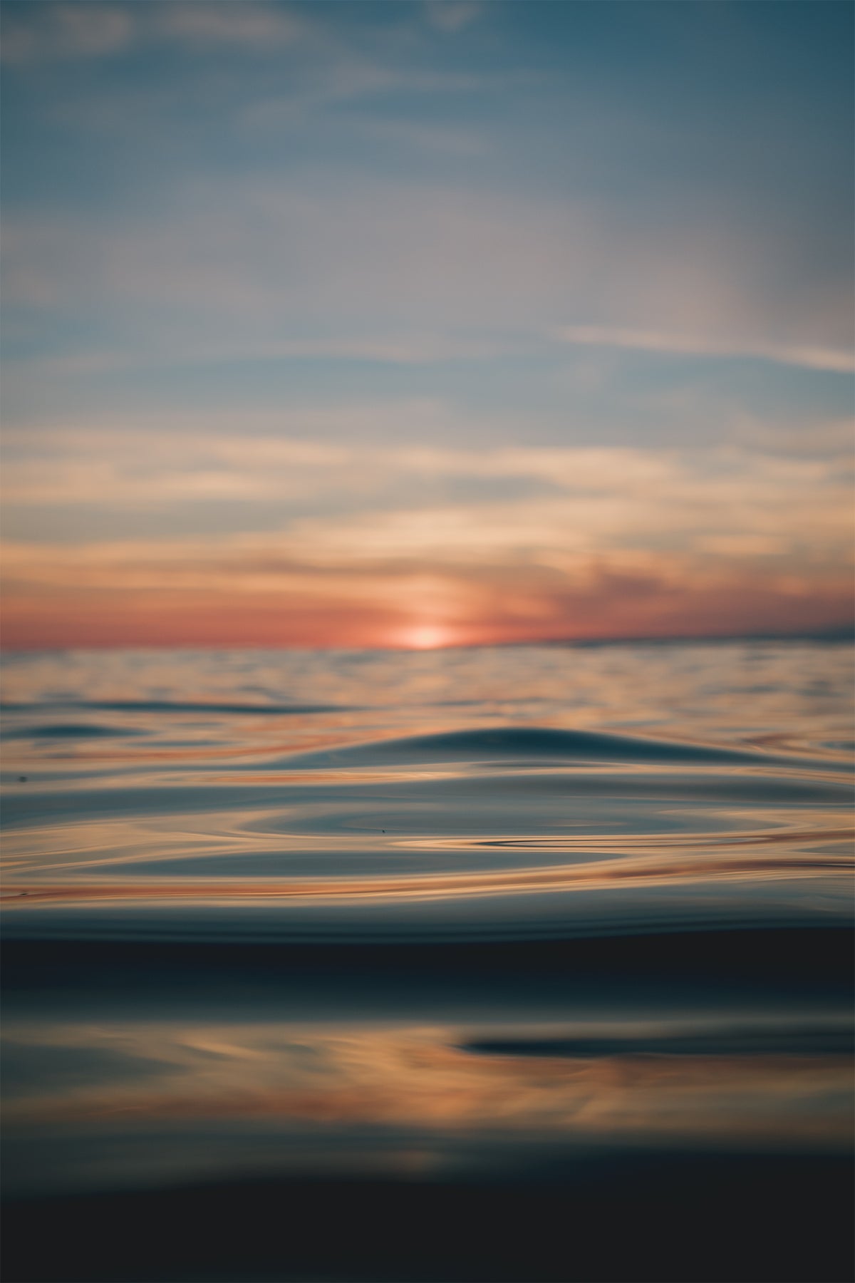 Sunset over a calm ocean with golden light reflecting on smooth water, photographed by Chris Hall in Newquay, Cornwall.