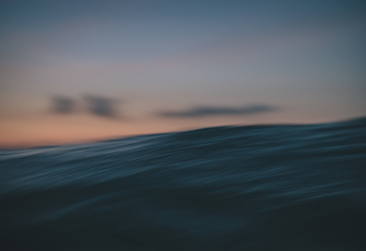 Photograph of an ocean wave at sunset taken from water level, with soft pastel skies and motion blur, part of The Sunset Journals series by Chris Hall available exclusively on The Lost Works gallery.