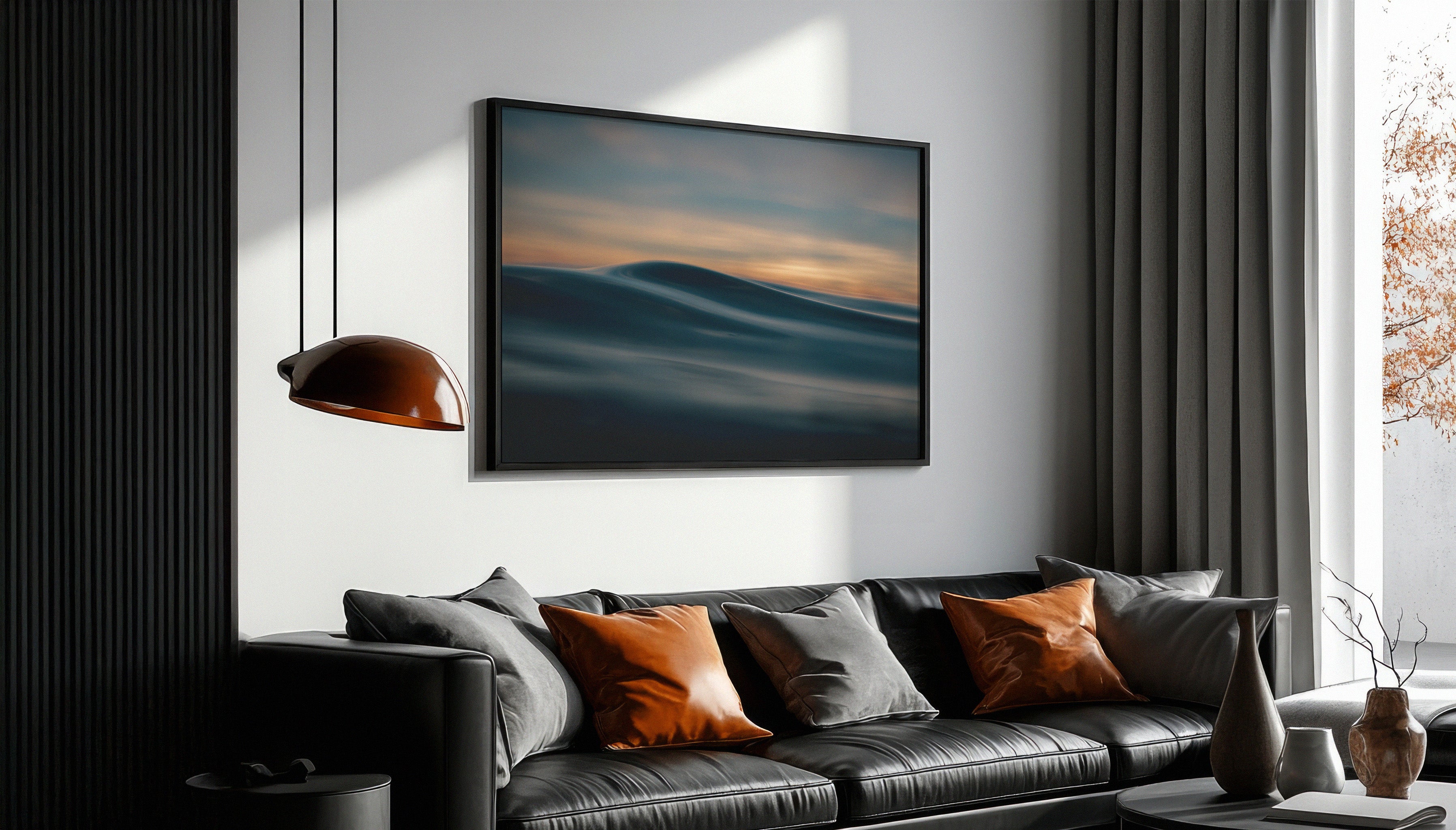 Chris Halls' fine art print hanging above a modern sofa in a large black frame, depicting a smooth, abstract ocean wave at sunset under soft golden skies, photographed at Fistral Beach.