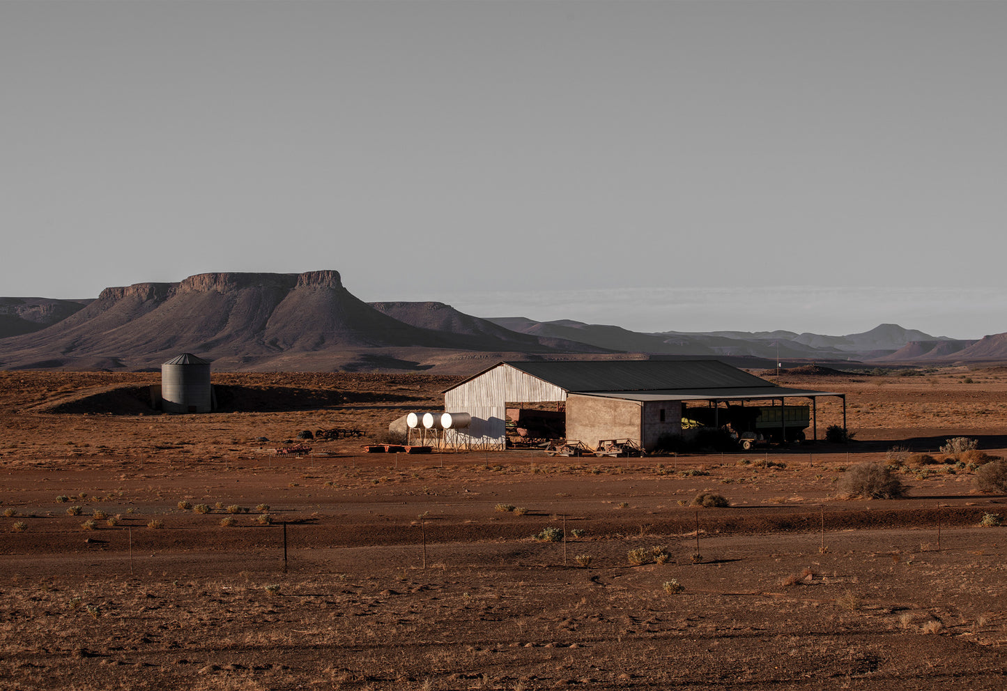 The desert landscape of the Karoo in red tones with metal farm buildings creating a striking fine art print by Charles Johnstone.