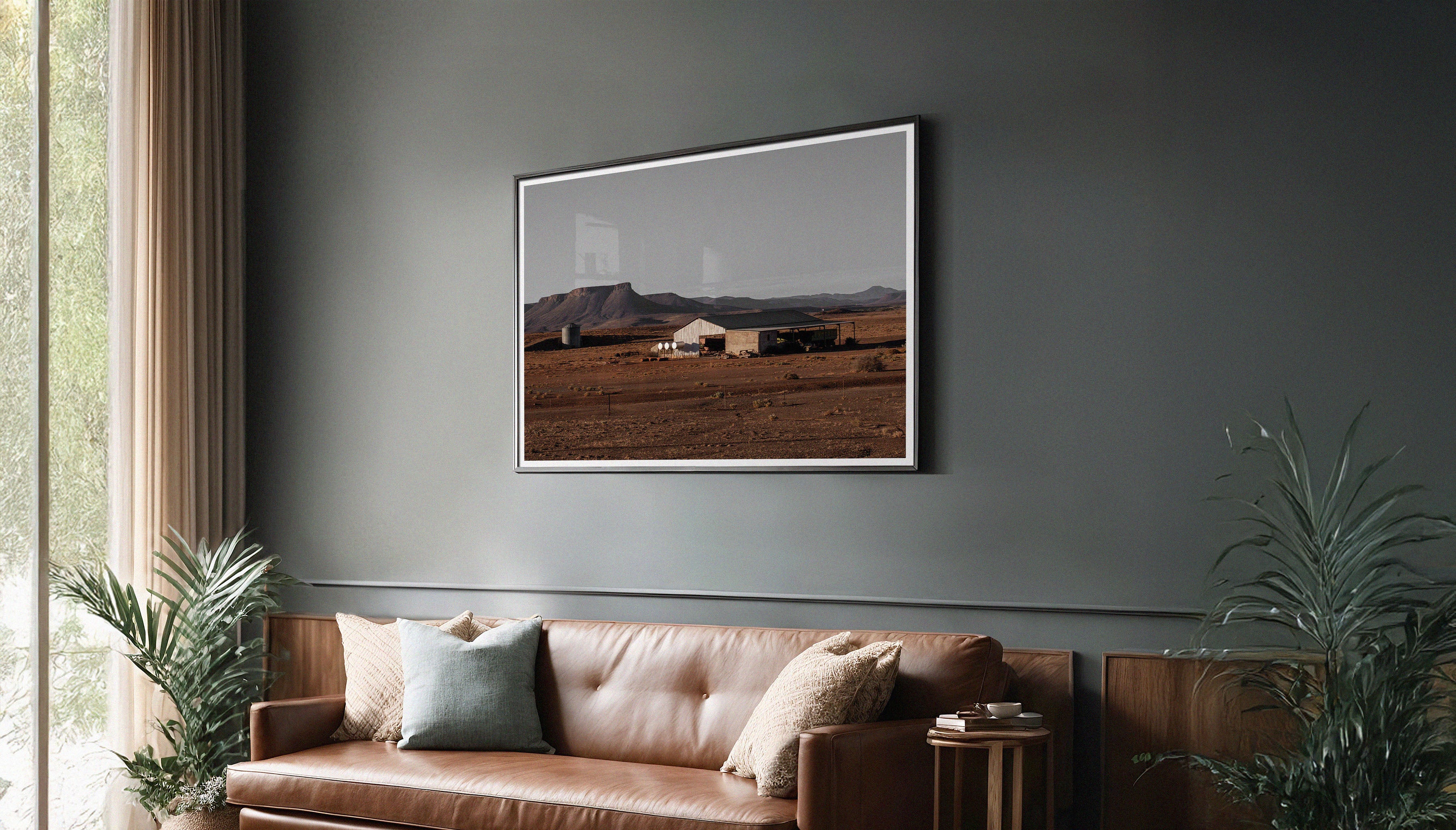Charles Johnstone's 'Farm in Karoo' fine art print, shown in a black frame with a mount, hanging on a dark wall showcasing the striking contrast with the red tones of the desert landscape.