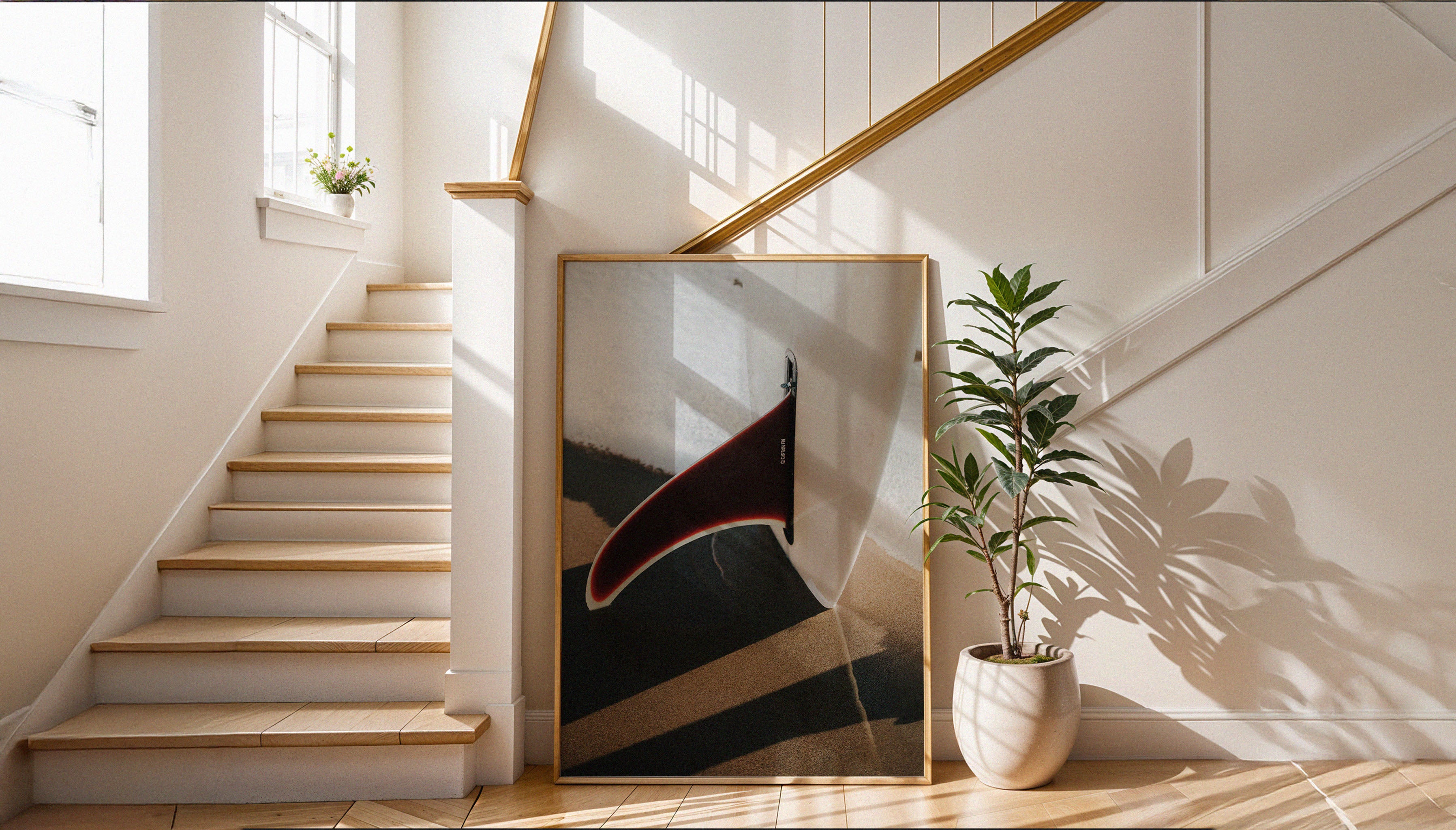 Sam Morris' 'Fin' - a red surfboard fin standing upright on golden sand - shown in situ as a framed fine art print leaning against a staircase. Purcahse from The Lost Works gallery.