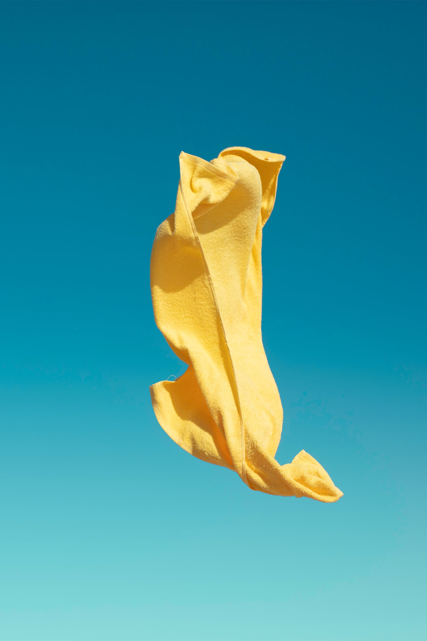 A yellow beach towel gets caught off guard on a windy day in the Algarve with a bright blue sky backdrop. A colourful fine art photography print by Will Bremridge, available exlcusively on The Lost Works.