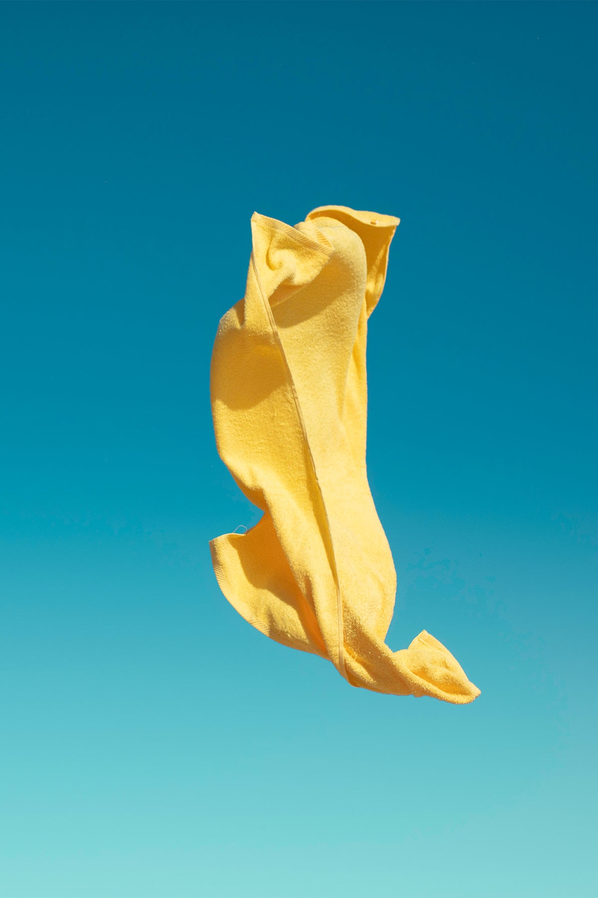 A yellow beach towel gets caught off guard on a windy day in the Algarve with a bright blue sky backdrop. A colourful fine art photography print by Will Bremridge, available exlcusively on The Lost Works.
