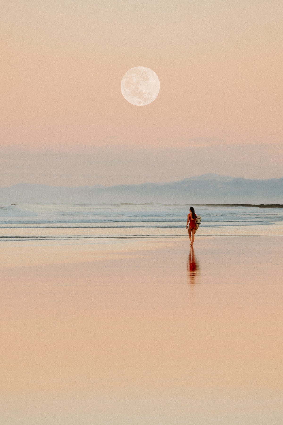 A surfer in a red wetsuit walking towards the surf under the full moon at sunrise - a fine art print by Evie Johnstone from Santa Teresa in Costa Rica.
