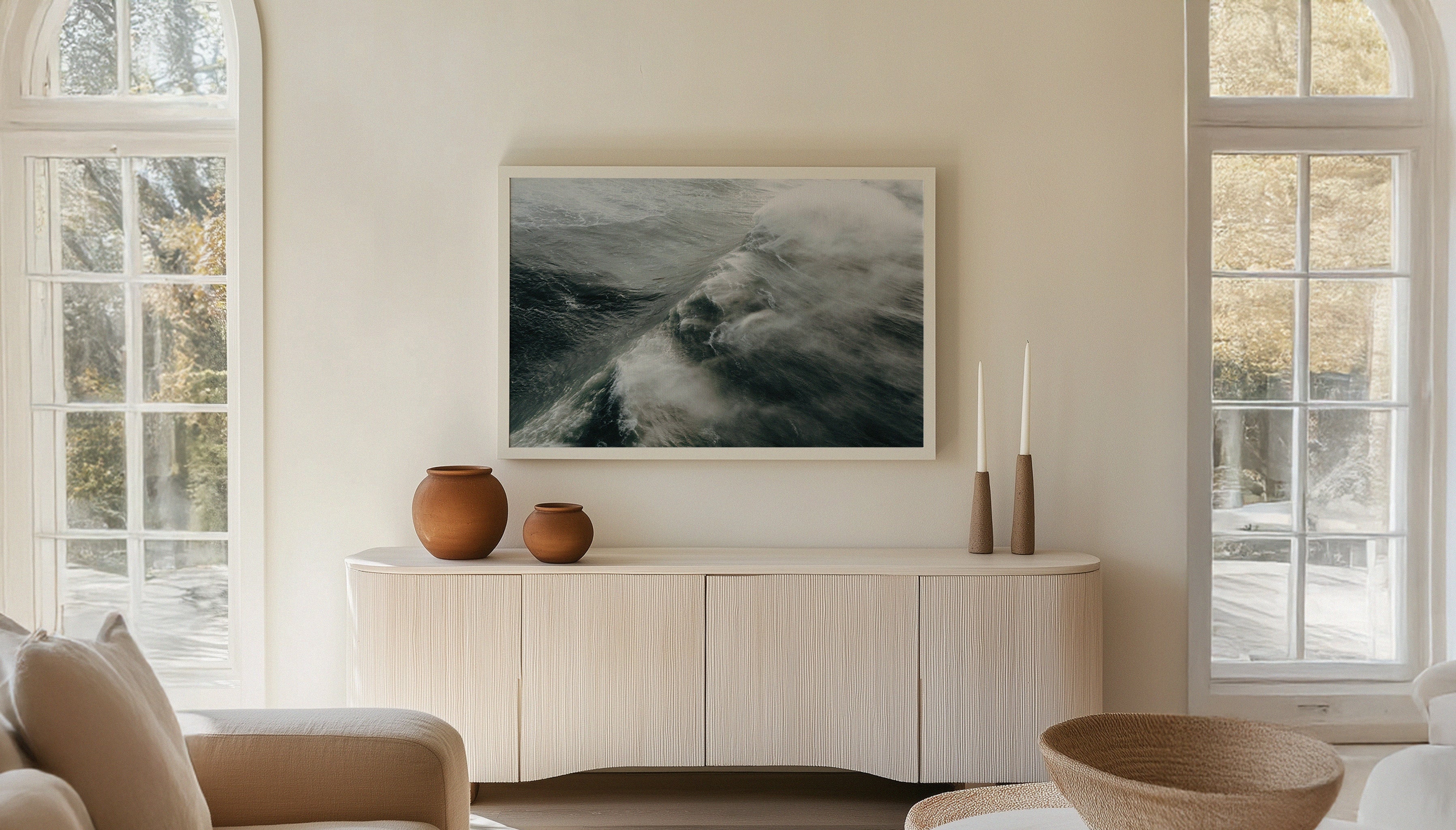 A fine art travel photograph by Sam Morris, depecting a massive 40ft wave crashing toward the shore at the legendary big wave surf spot Nazaré, shown in a white frame in a Scandi living room.