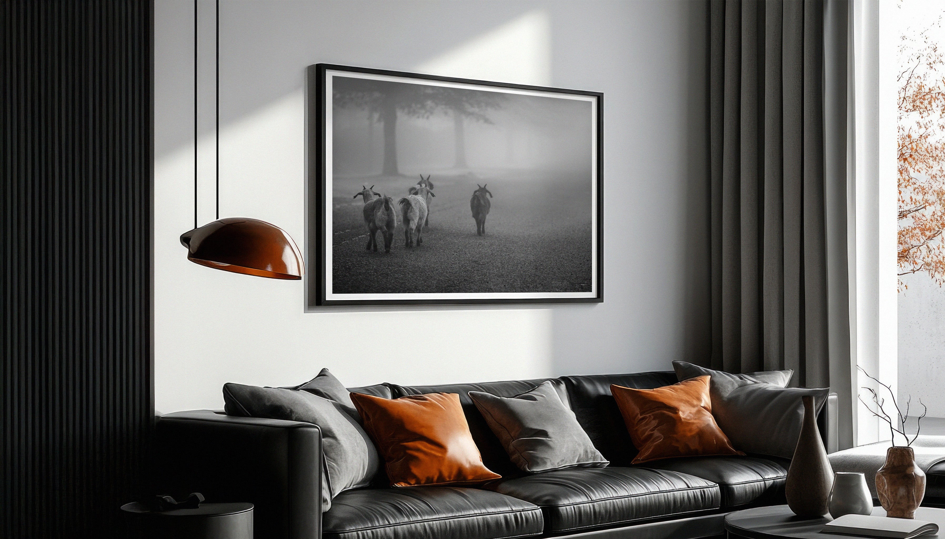Charles Johnstone's fine art print GOATS IN THE MIST displayed in a black frame with a white border, hanging above a black sofa in a modern living room.