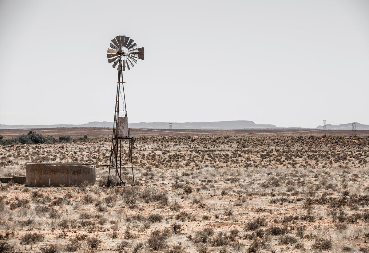A typical farm scene in the Karoo showing a 'windpomp' or windpump in an arid African landscape - fine art print by Charles Johnstone.