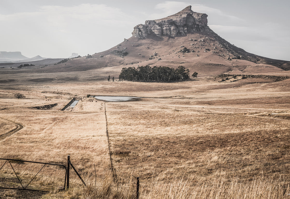 A rugged hill formation - otherwise known as a koppie - stands tall in dry grassland in KwaZulu-Natal in this typical African landscape scene, captured as a fine art print by Charles Johnstone.