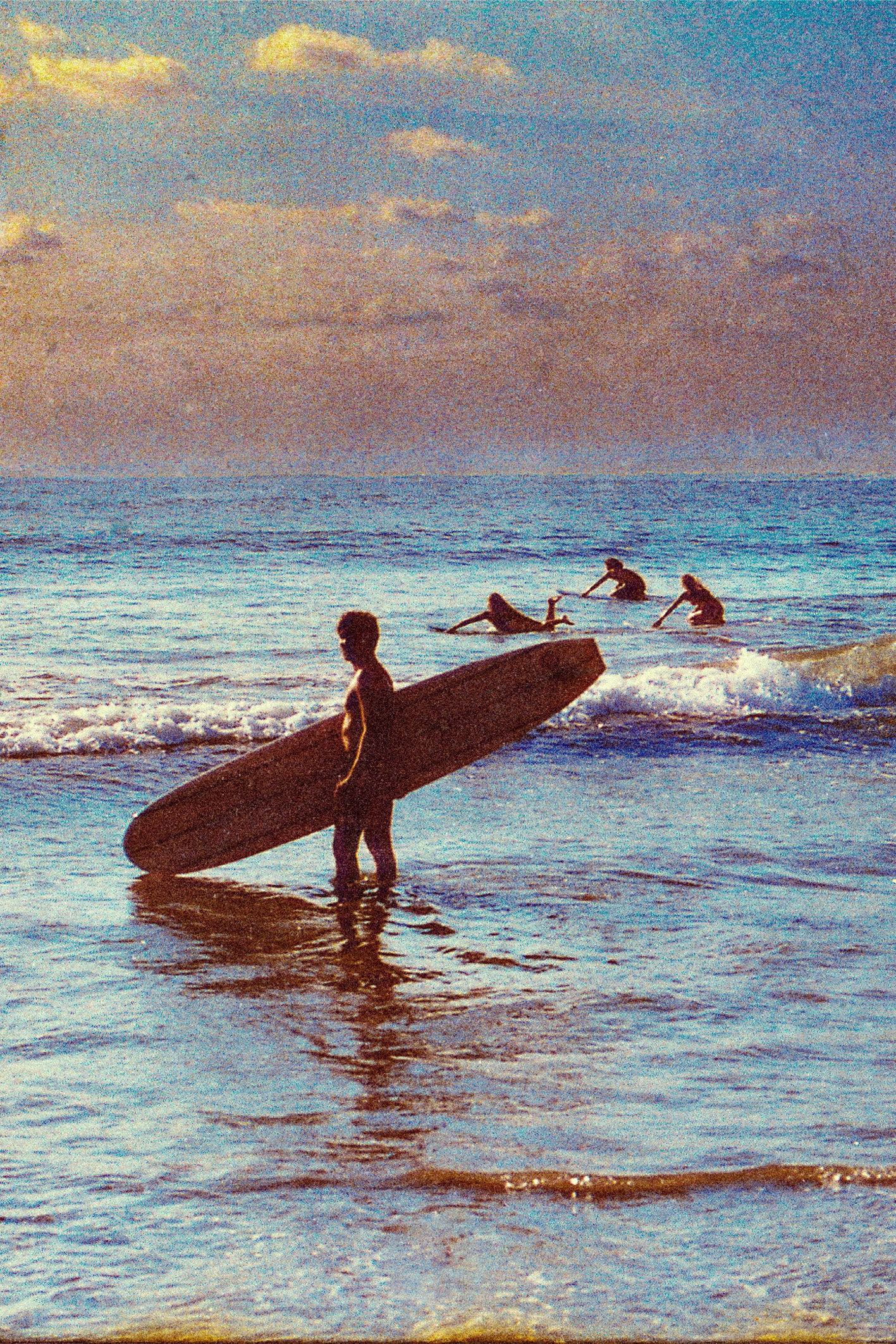 Silhouetted surfer holding a longboard at sunset in Santa Teresa, Costa Rica, with three surfers paddling in the background, captured by surf photographer Ez Rivero.