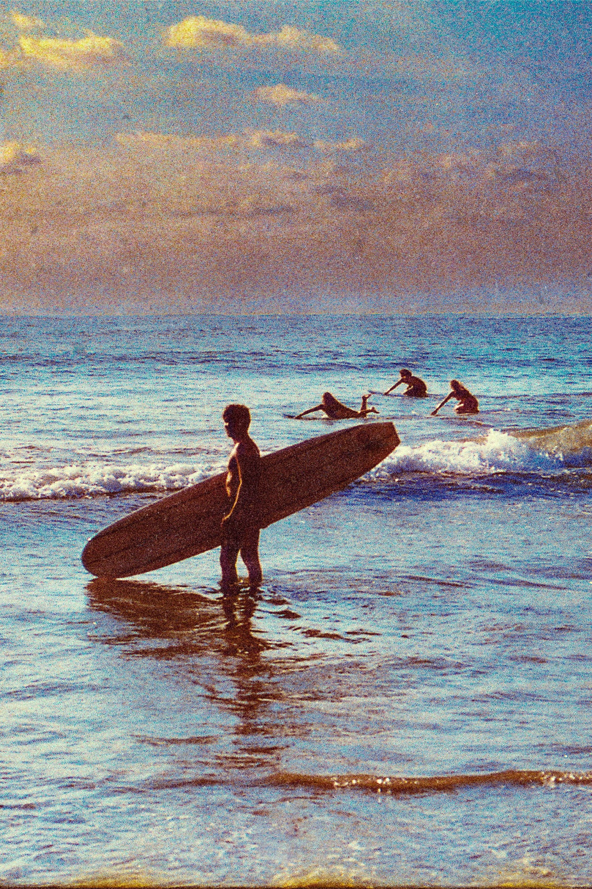 Silhouetted surfer holding a longboard at sunset in Santa Teresa, Costa Rica, with three surfers paddling in the background, captured by surf photographer Ez Rivero.