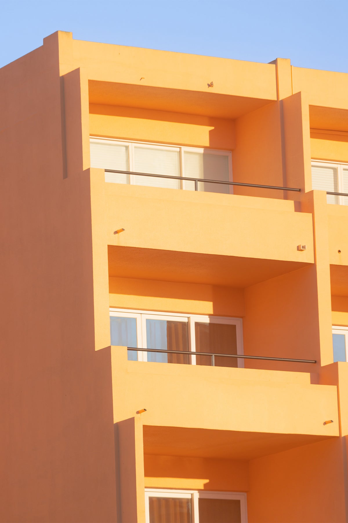The Portuguese sunshine makes an apartment block glow with muted mango delight against the blue sky. Straight clean lines bring calm and serenity. A piece of wall art by Will Bremridge guaranteed to brighten any space, available to purchase on The Lost Works as a fine art print.