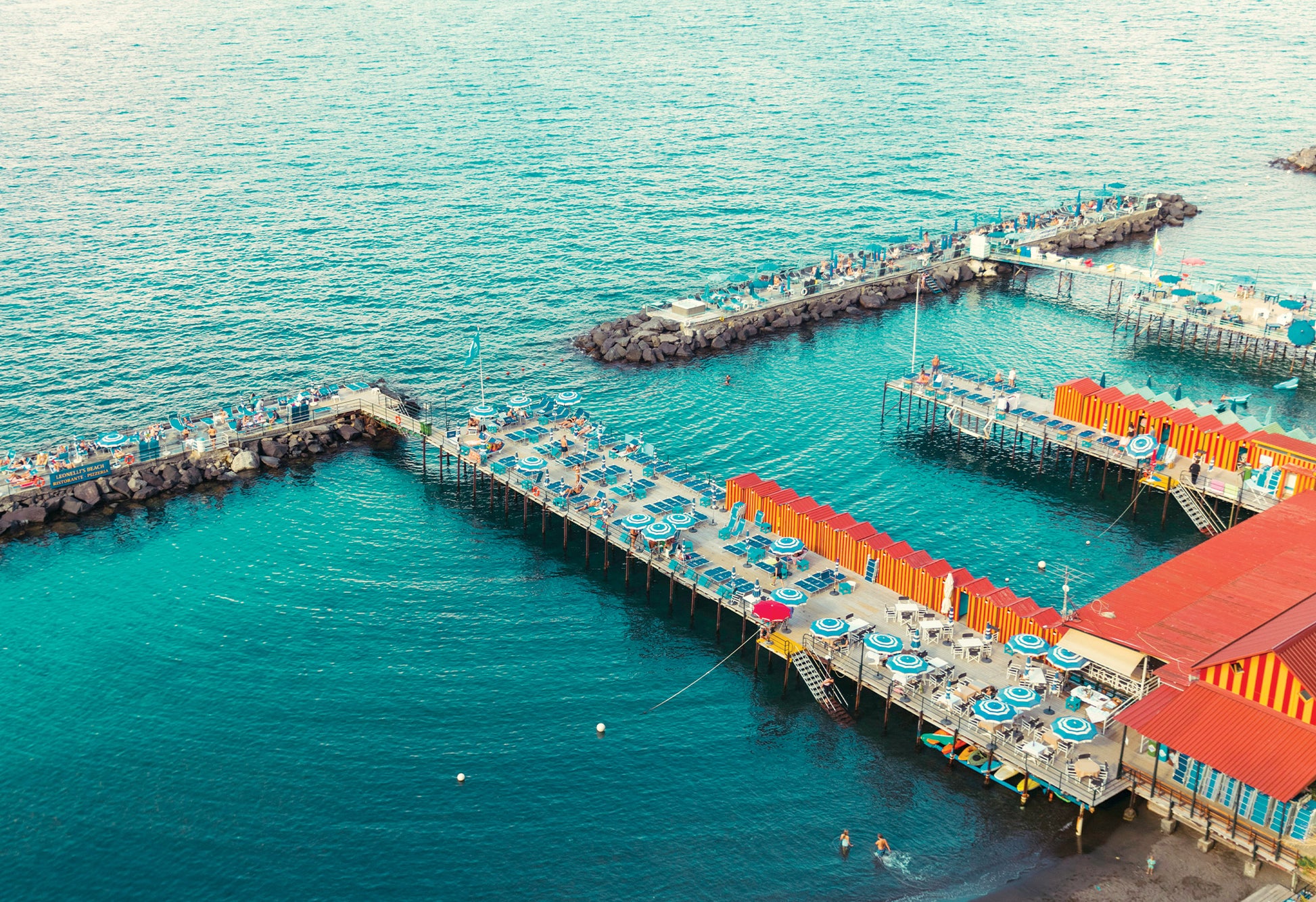 A photograph by Will Bremridge looking down to Marina Grande on the Amalfi Coast. The iconic blue of the Amalfi sea plays backdrop to playful red and yellow stripes. Available to purchase as a fine art print with free framing service from The Lost Works.