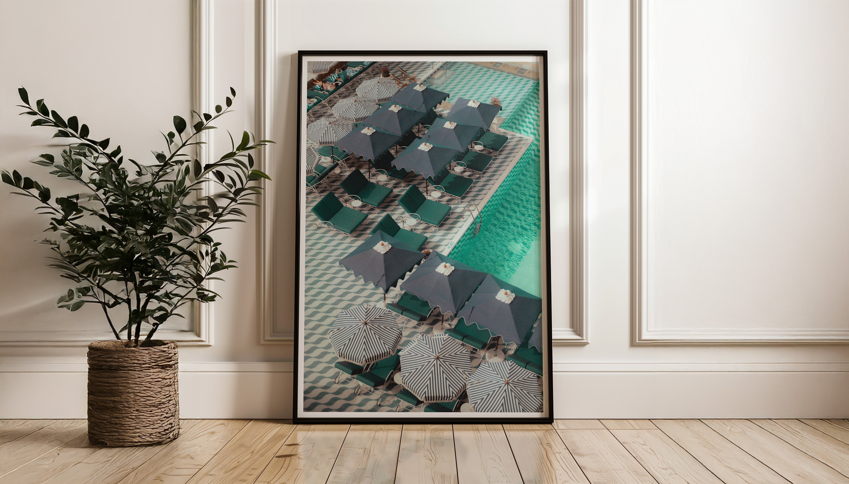 A wide shot of PATTERNS, a photography print by Evie Johnstone, in a large black frame leaning against a white wall on a wooden floor and with a plant in a basket nearby.