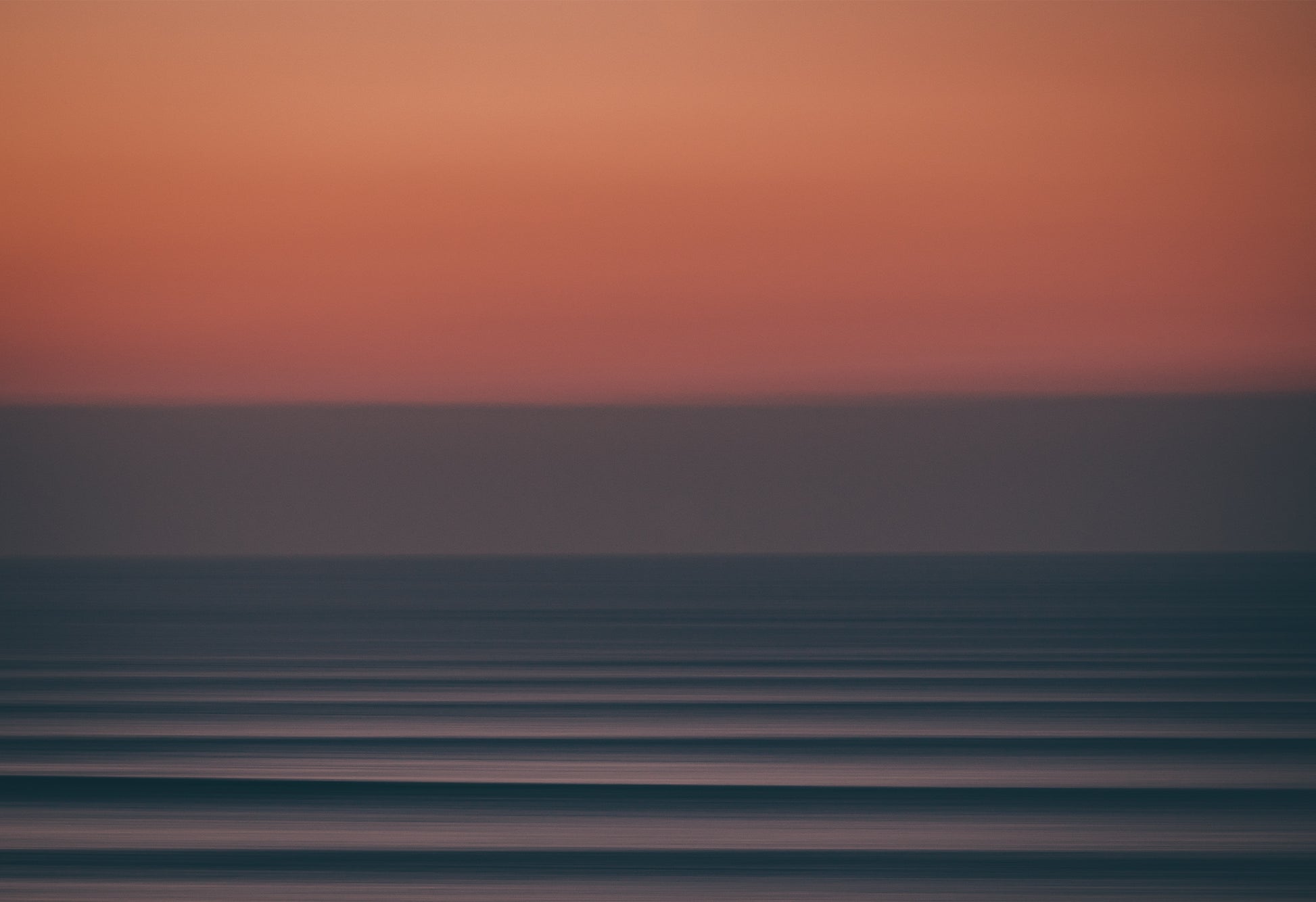 Long-exposure photograph of a moody Atlantic sunset at Fistral Beach, Cornwall, showing abstract horizontal waves beneath a deep red and purple sky.