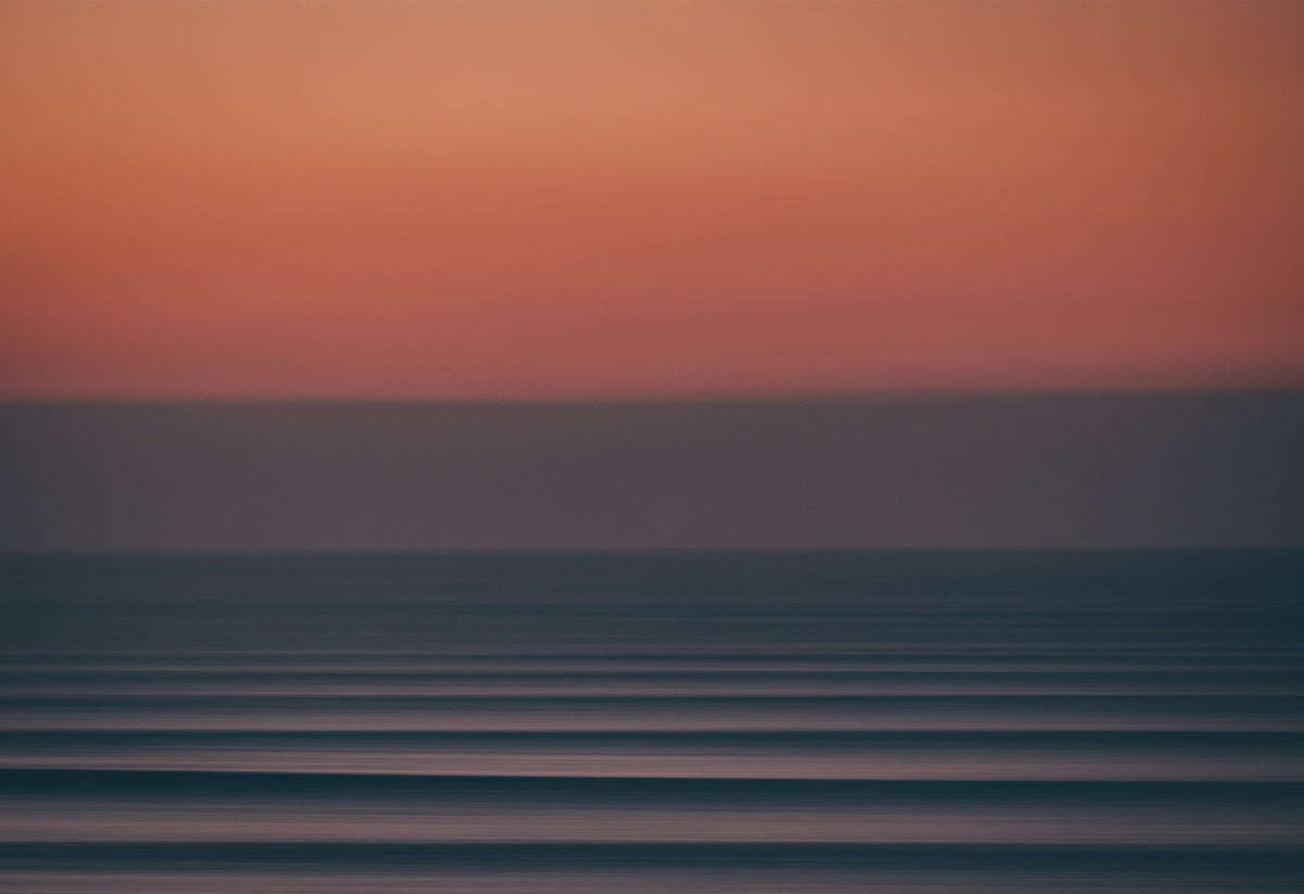 Long-exposure photograph of a moody Atlantic sunset at Fistral Beach, Cornwall, showing abstract horizontal waves beneath a deep red and purple sky.