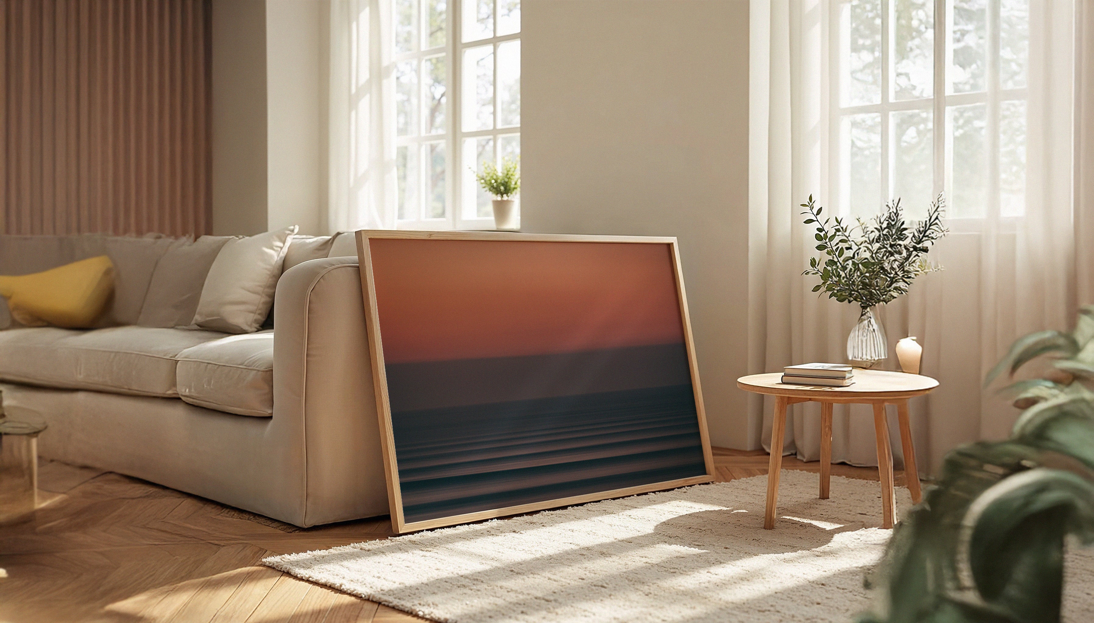 Chris Hall's SEA PAINTING 002 - a long-exposure photograph of a moody Atlantic sunset at Fistral Beach, showing abstract horizontal waves beneath a deep red and purple sky - in a wooden frame leaning against a sofa in a Scandi-style interior.