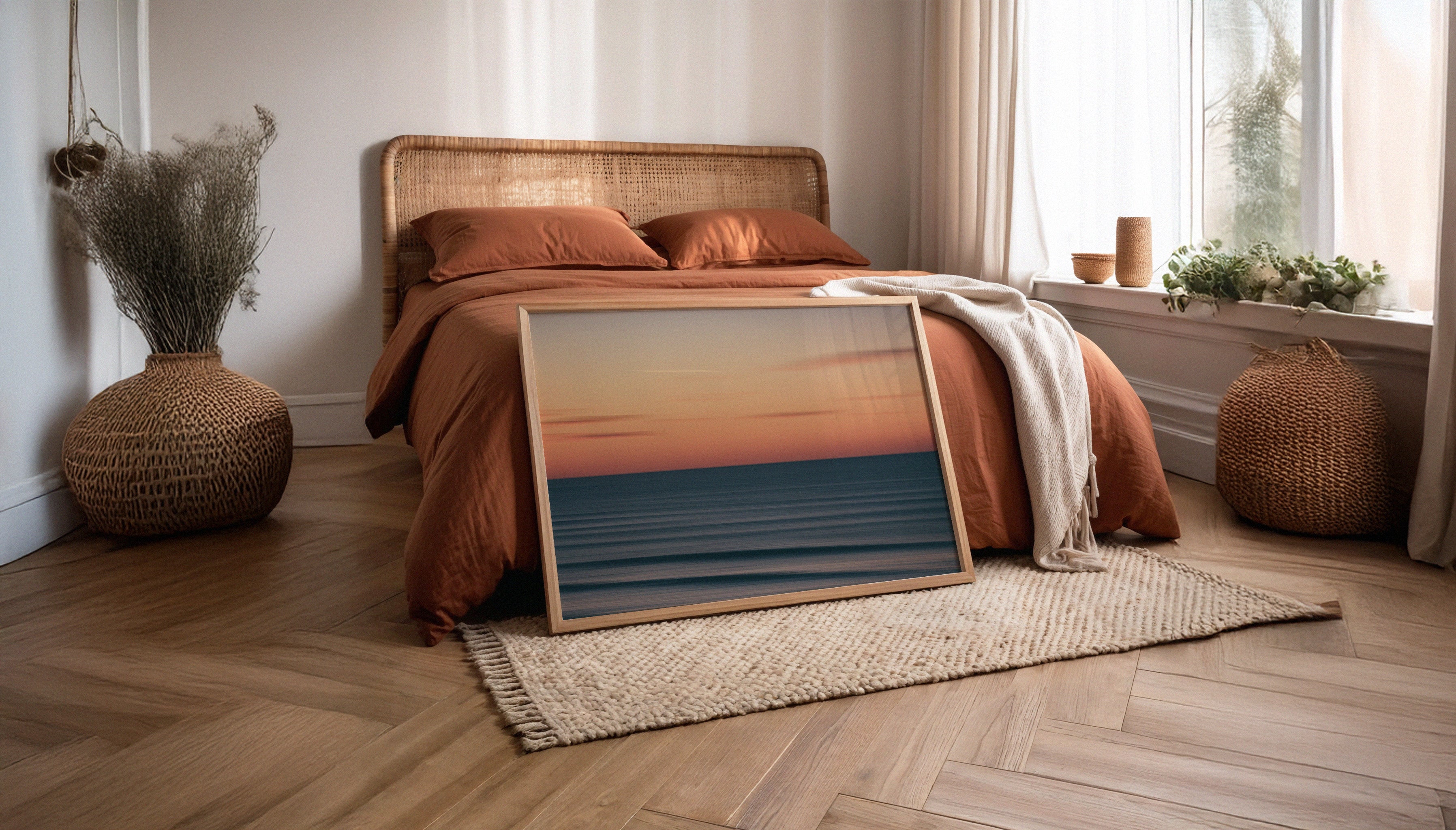 Chris Hall's SEA PAINTING 001 - an abstract long-exposure photograph of a sunset over the ocean at Fistral Beach, Newquay, with soft pastel tones and blurred waves - in a wooden frame leaning agaisnt a rust coloured linen bed.