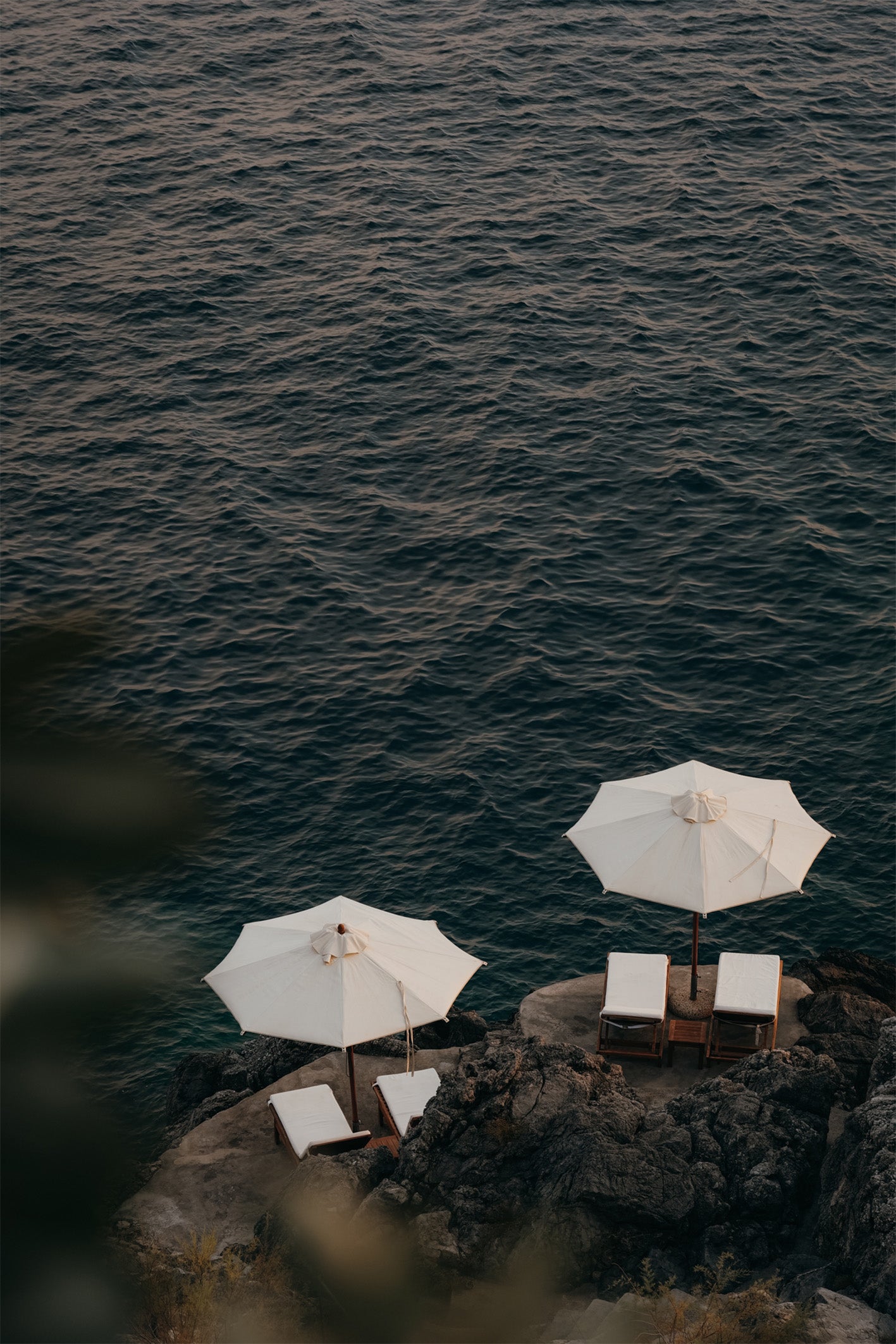 The crisp white of two umbrellas stand in striking contrast to the shimmering, deep blue water of the Almalfi Coast, Italy. A photograph by Hannes Kläger, available to buy as a framed, ready-to-hang fine art print.