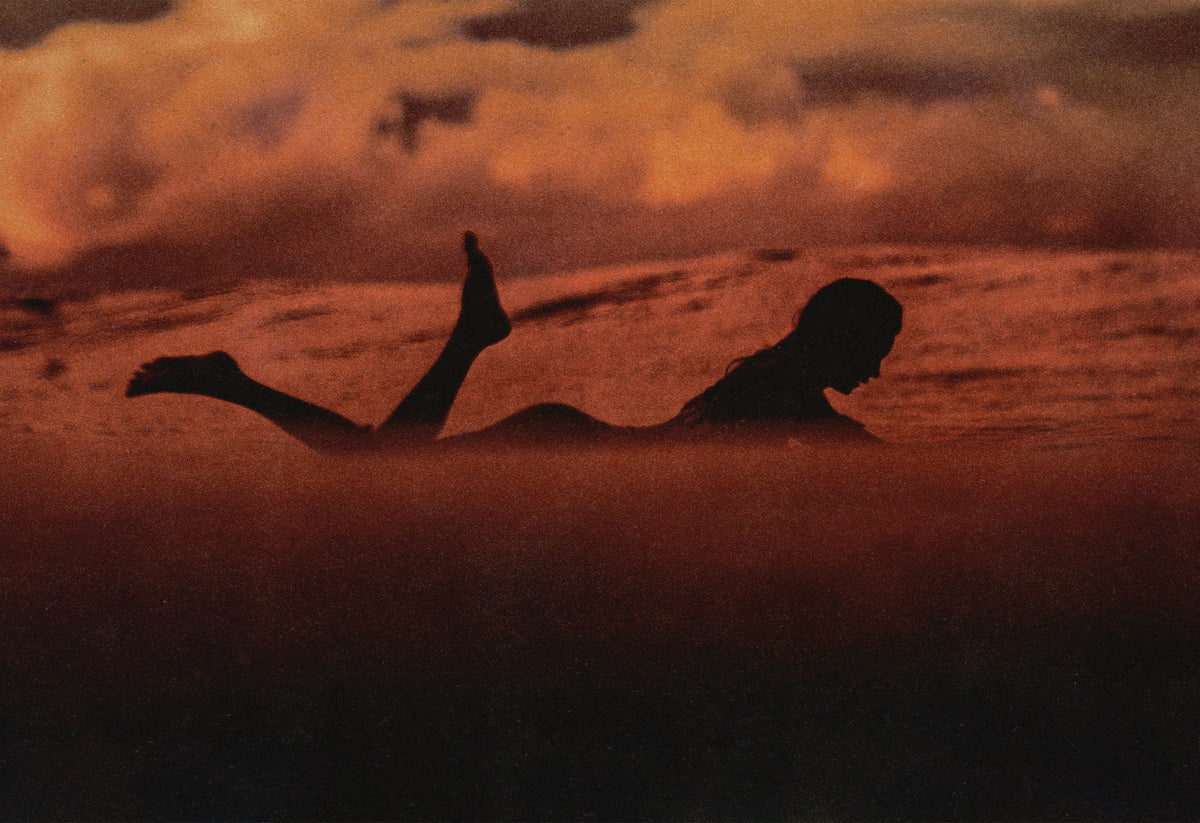 Silhouette of a surfer paddling at sunset with deep red and orange hues over the ocean in Santa Teresa, captured by Ez Rivero – fine art travel photography print.