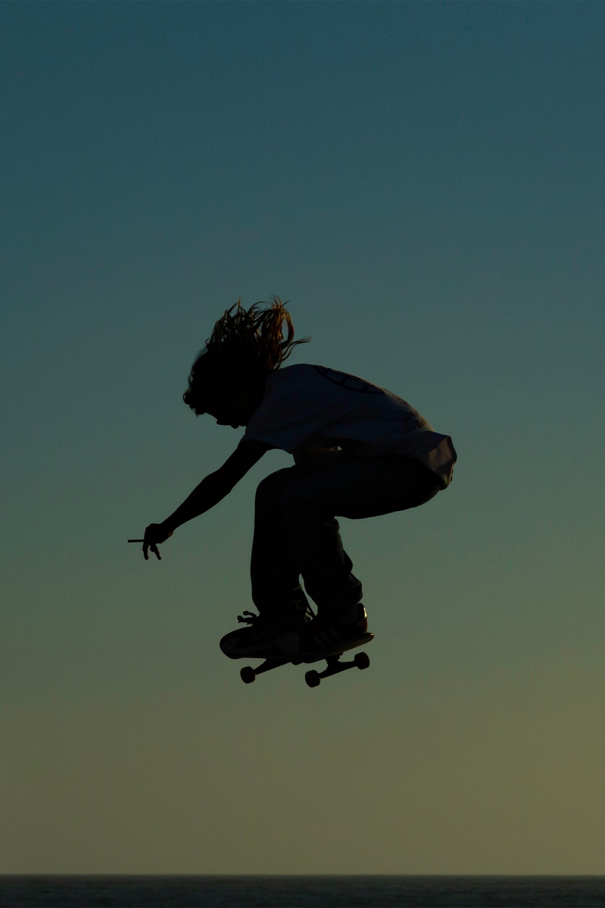Iconic skateboarding photo of a silhouetted skater with a lit cigarette, catching air at Venice Skatepark - SMOKE by Craig Hubbard, shot at golden hour.