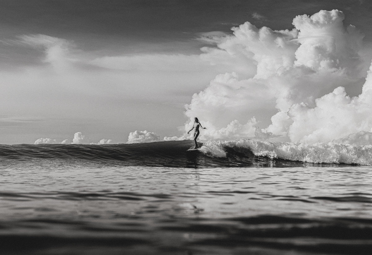 Black and white photo of a female surfer riding a wave beneath towering cumulus clouds in Santa Teresa, Costa Rica, captured by Ez Rivero.