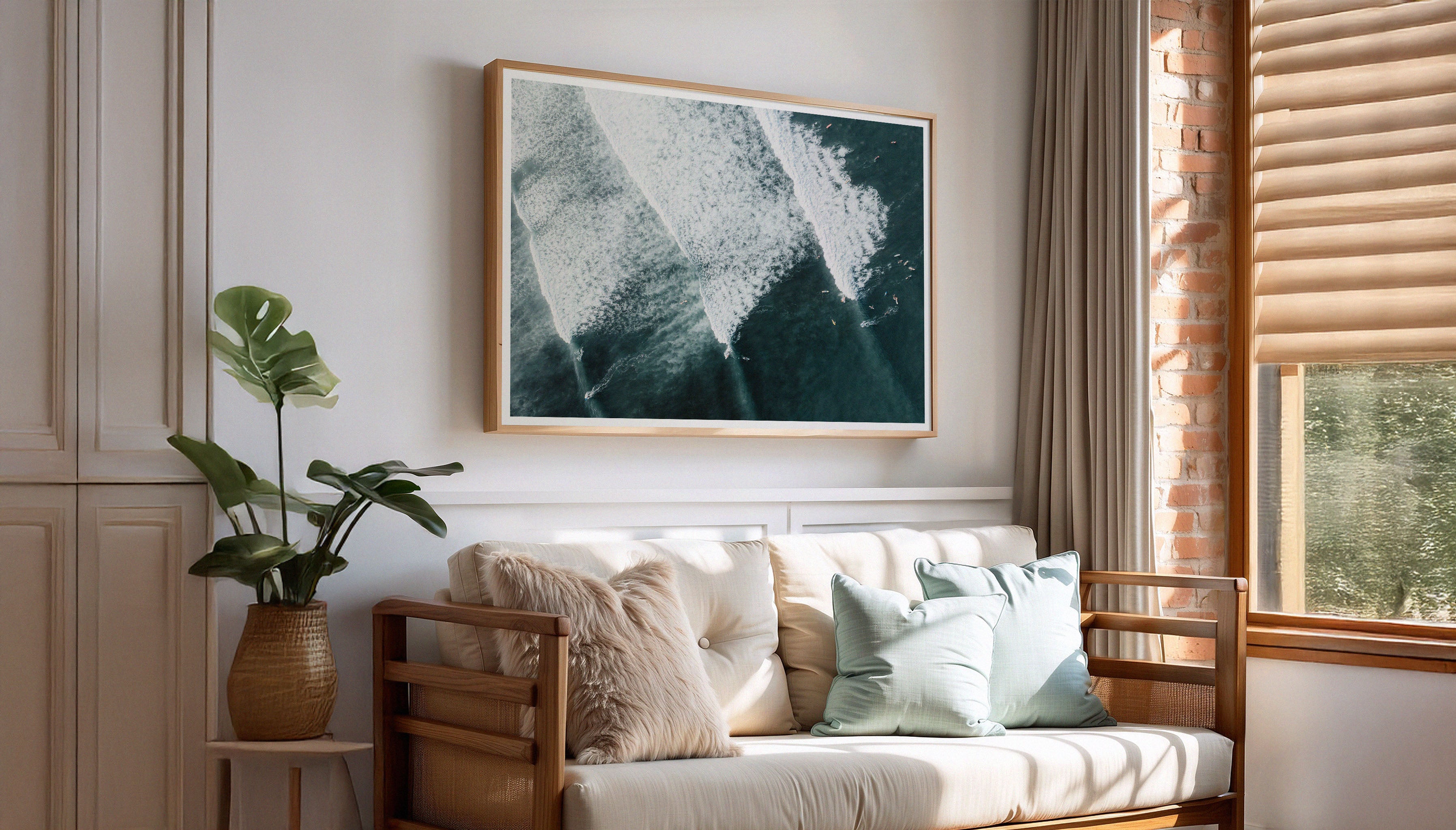 Sam Morris' aerial shot of surfers riding turquoise waves off the coast of Bali, shown in a boho living room setting. A travel-inspired fine art photograph available on The Lost Works.