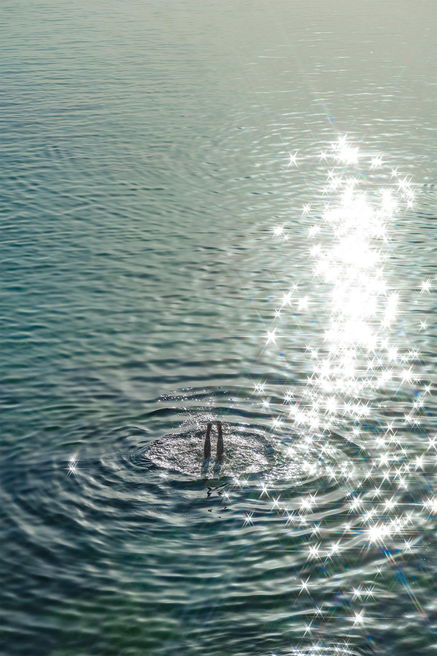 Glistening turquoise sea engulfs a pair of legs, a diver lost to the ripples - a fine art print from Ibiza by Evie Johnstone.