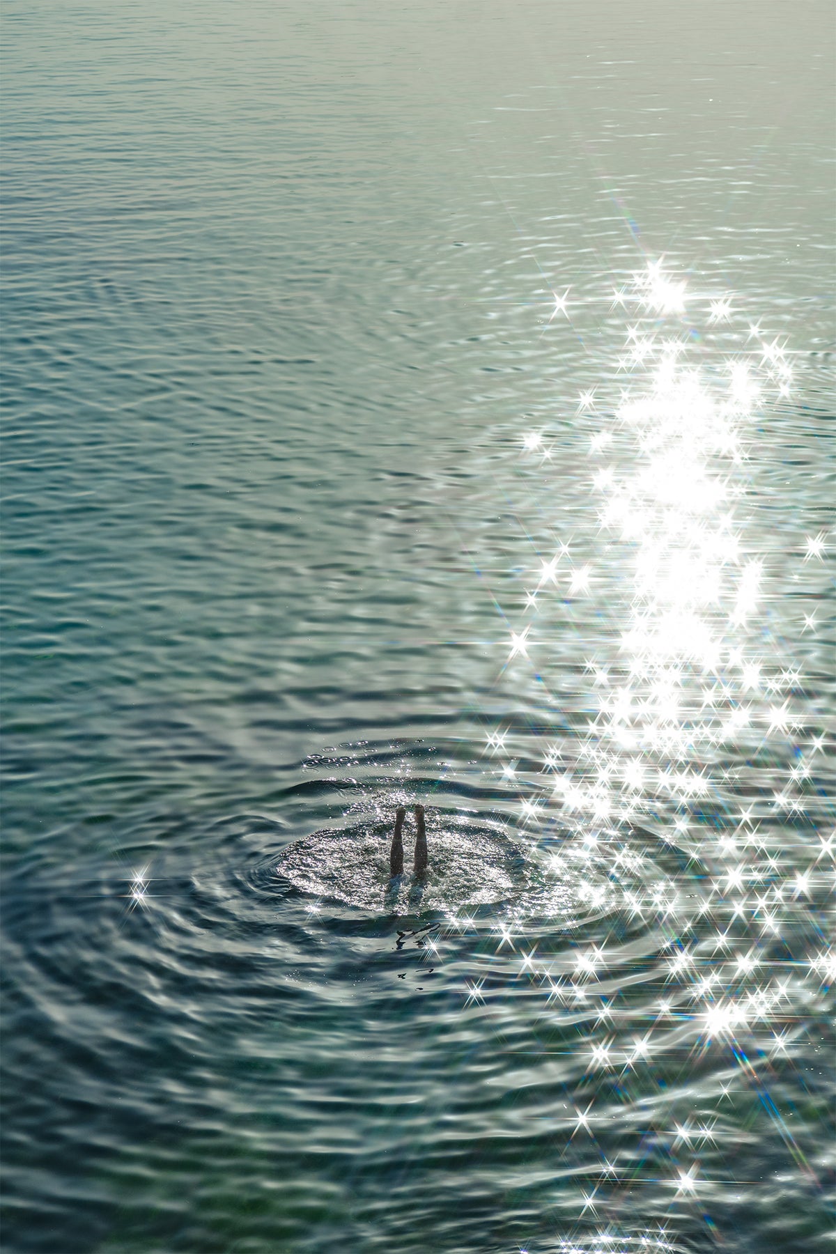 Glistening turquoise sea engulfs a pair of legs, a diver lost to the ripples - a fine art print from Ibiza by Evie Johnstone.