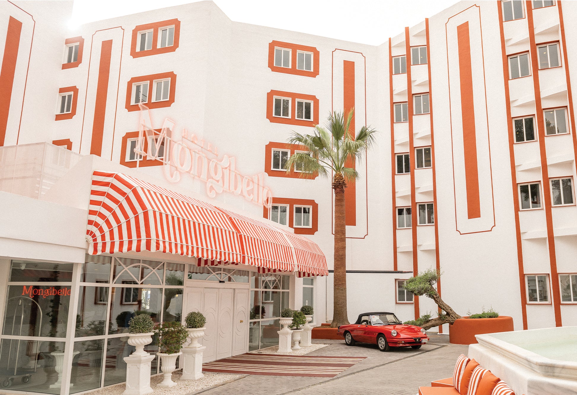 A retro themed hotel with red and white striped awning, palm trees, and a red Alfa Romeo car parked outside, captured by Evie Johnstone and available as a ready-to-hang framed print.