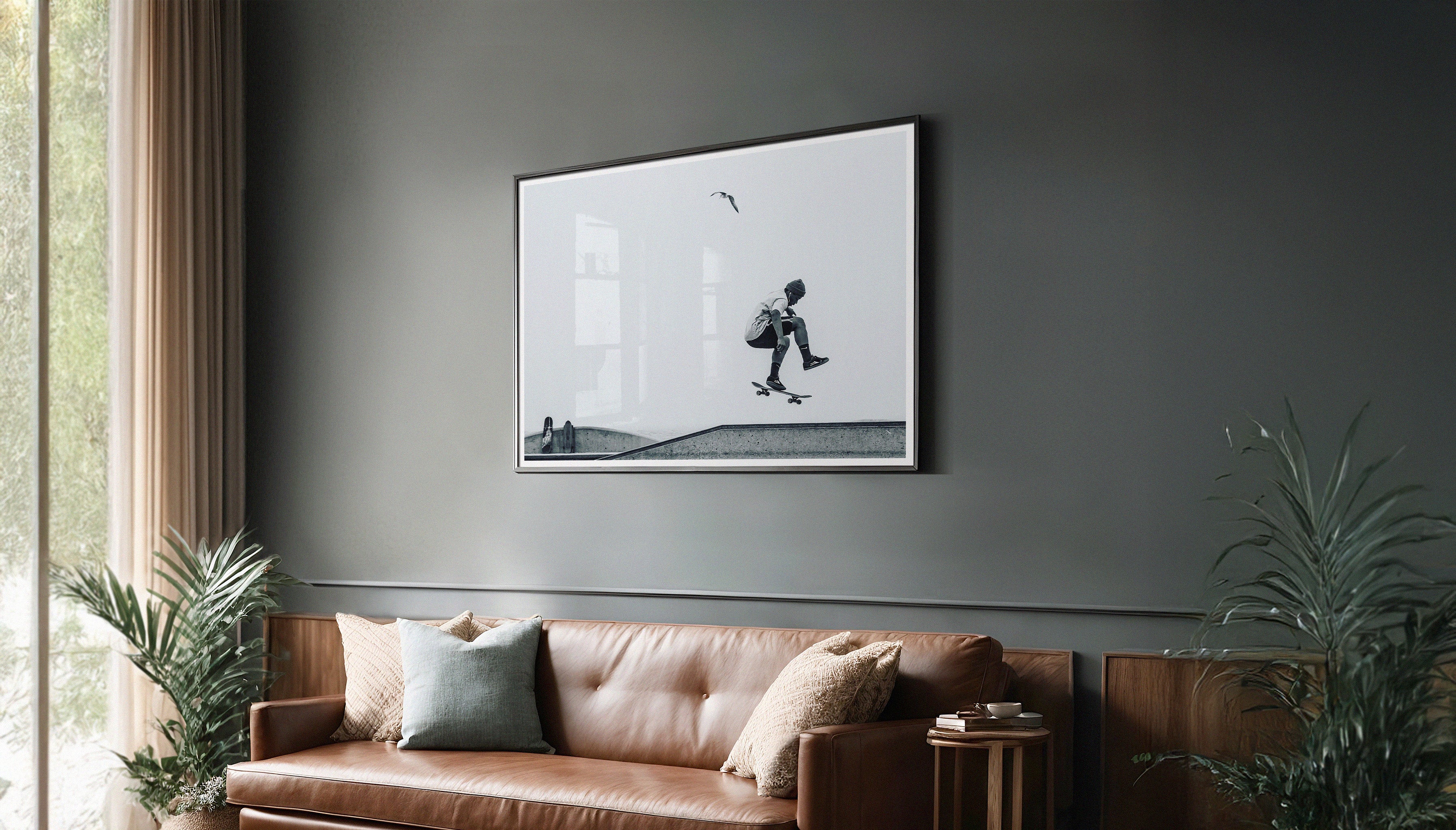Modern interior with a framed black-and-white skateboarding print titled “The Bird” by Craig Hubbard displayed on a muted grey wall above a leather couch.