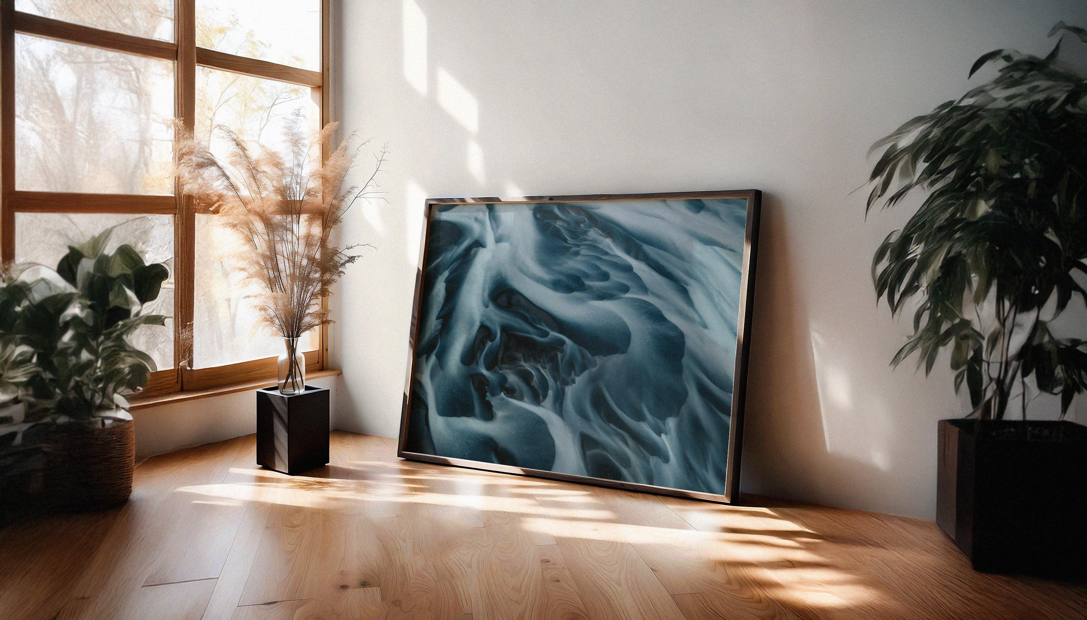The dramatic fine art print by Sam Morris in a black frame, capturing an aerial view of an Icelandic river flowing toward the sea, with blue and white patterns.